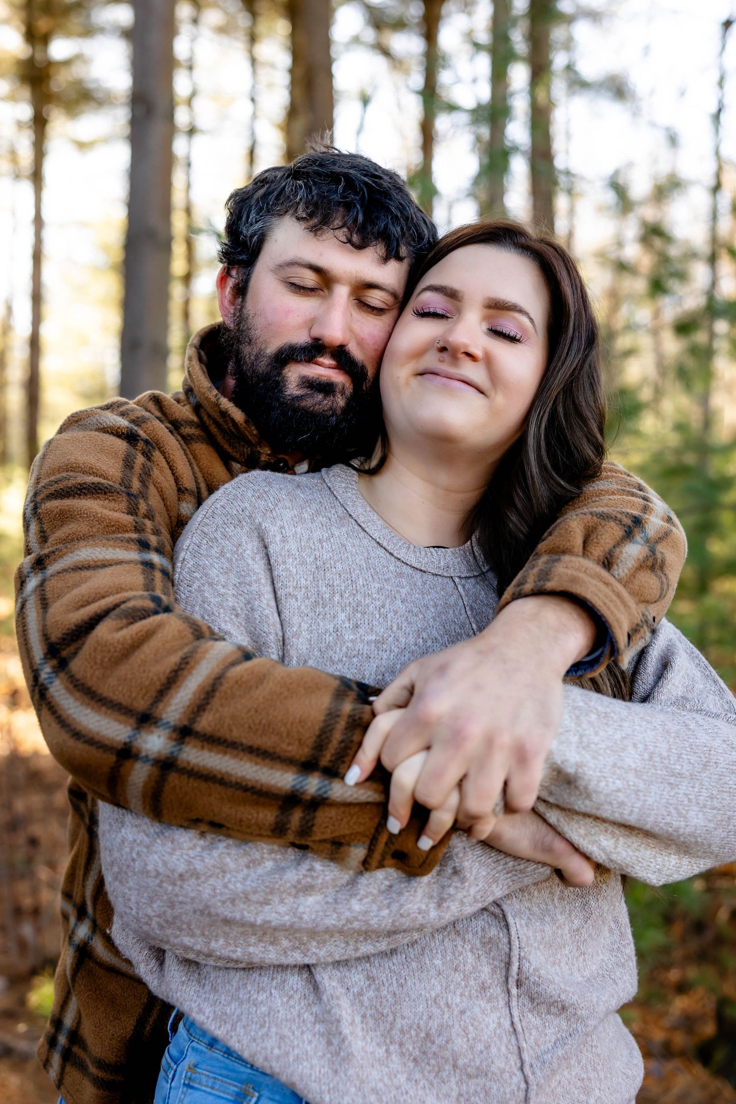 An intimate embrace between a couple wearing casual attire in a sunlit forest.