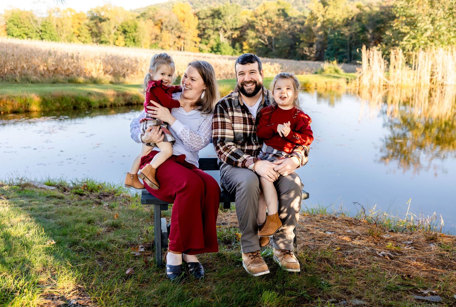 Happy family sits together on wooden bench near autumn lake with golden light.