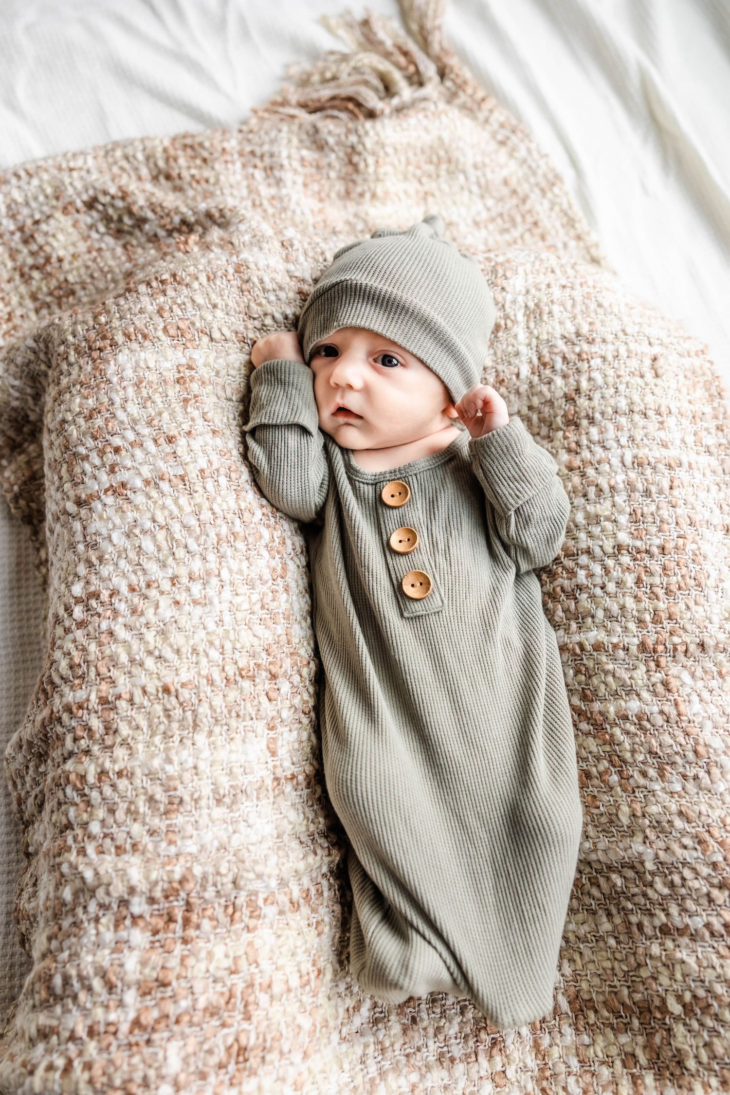 Baby in cozy grey outfit stretching arms while lying on textured blanket.