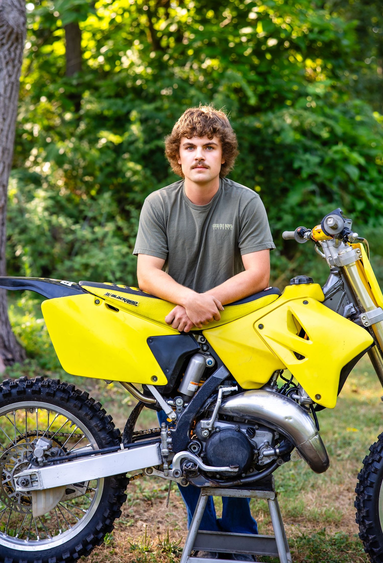 Bright yellow motocross bike on display stand with rider in casual attire.