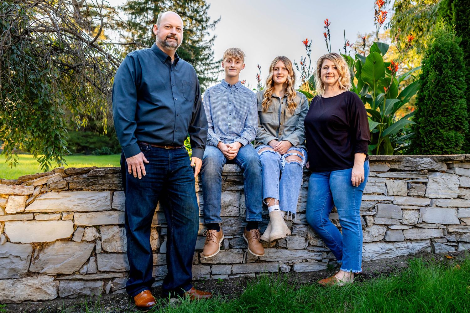 A family group sits and stands on a stone wall in a garden setting.