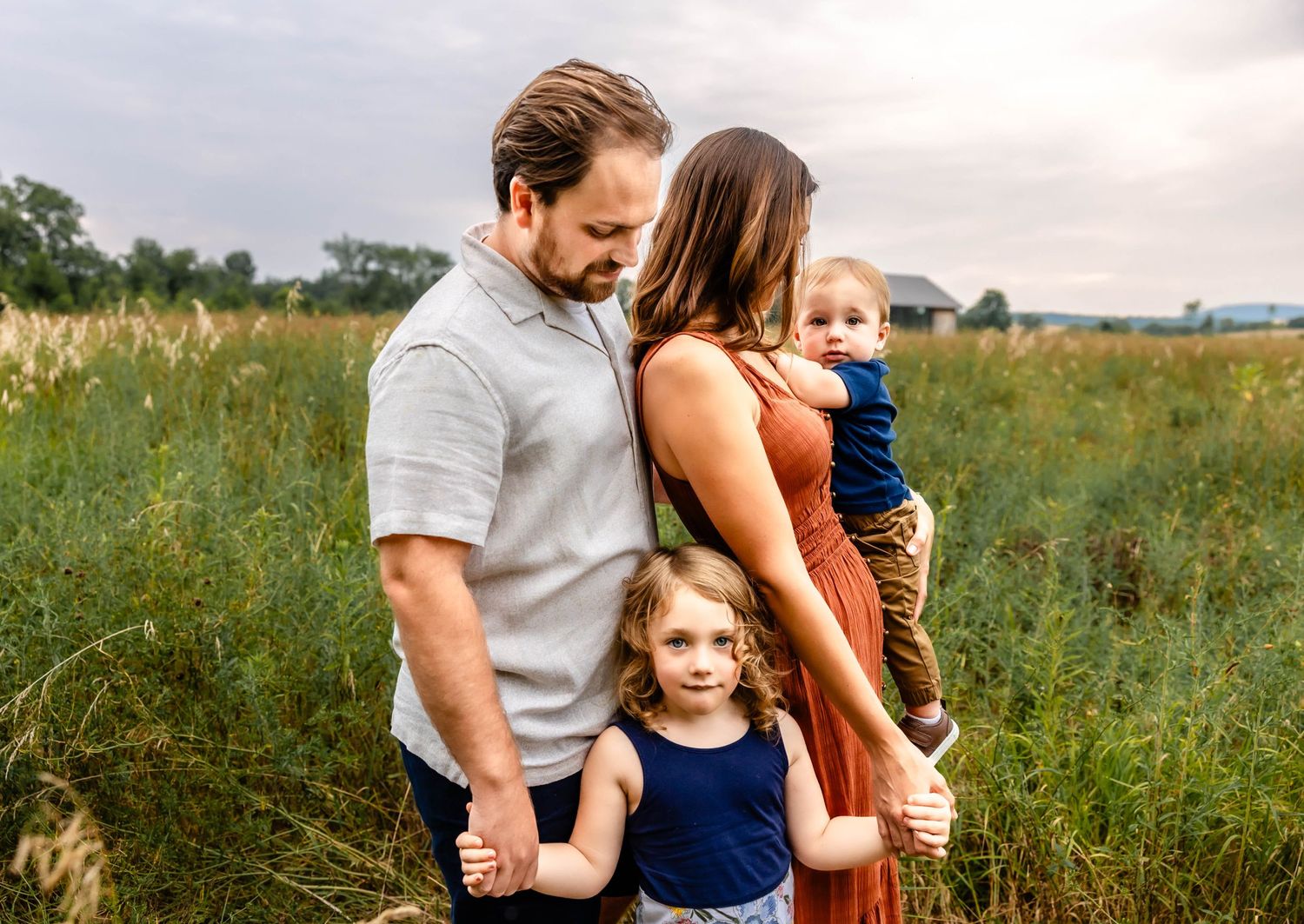 Family poses together in an open meadow with a cloudy sky backdrop wearing coordinated outfits.