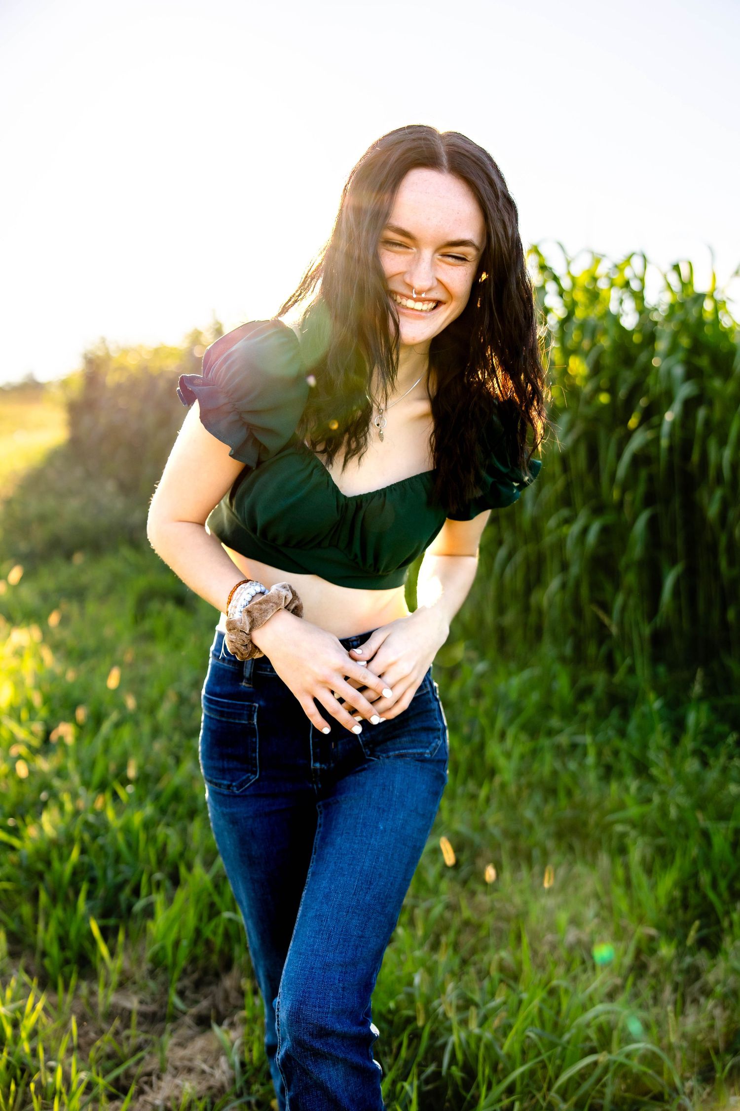 Golden hour portrait with laughter and greenery featuring casual denim and a dark top.
