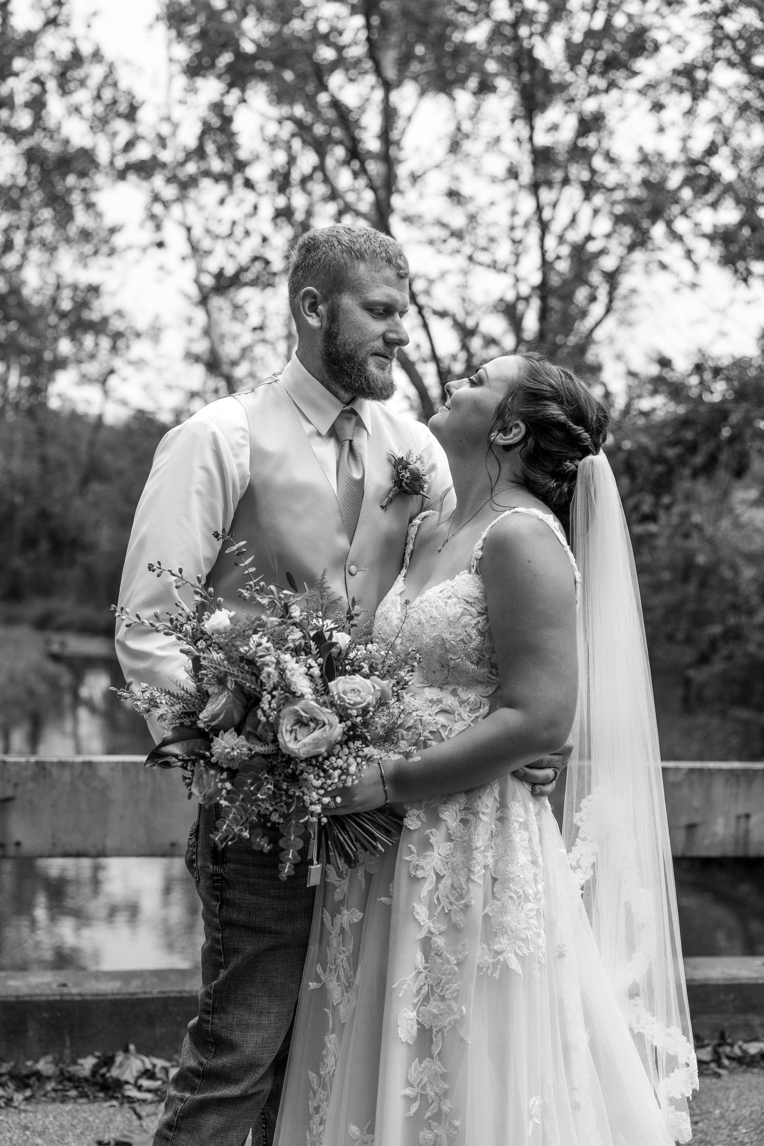 Wedding couple shares a joyful moment outdoors with a beautiful floral bouquet against a natural backdrop.
