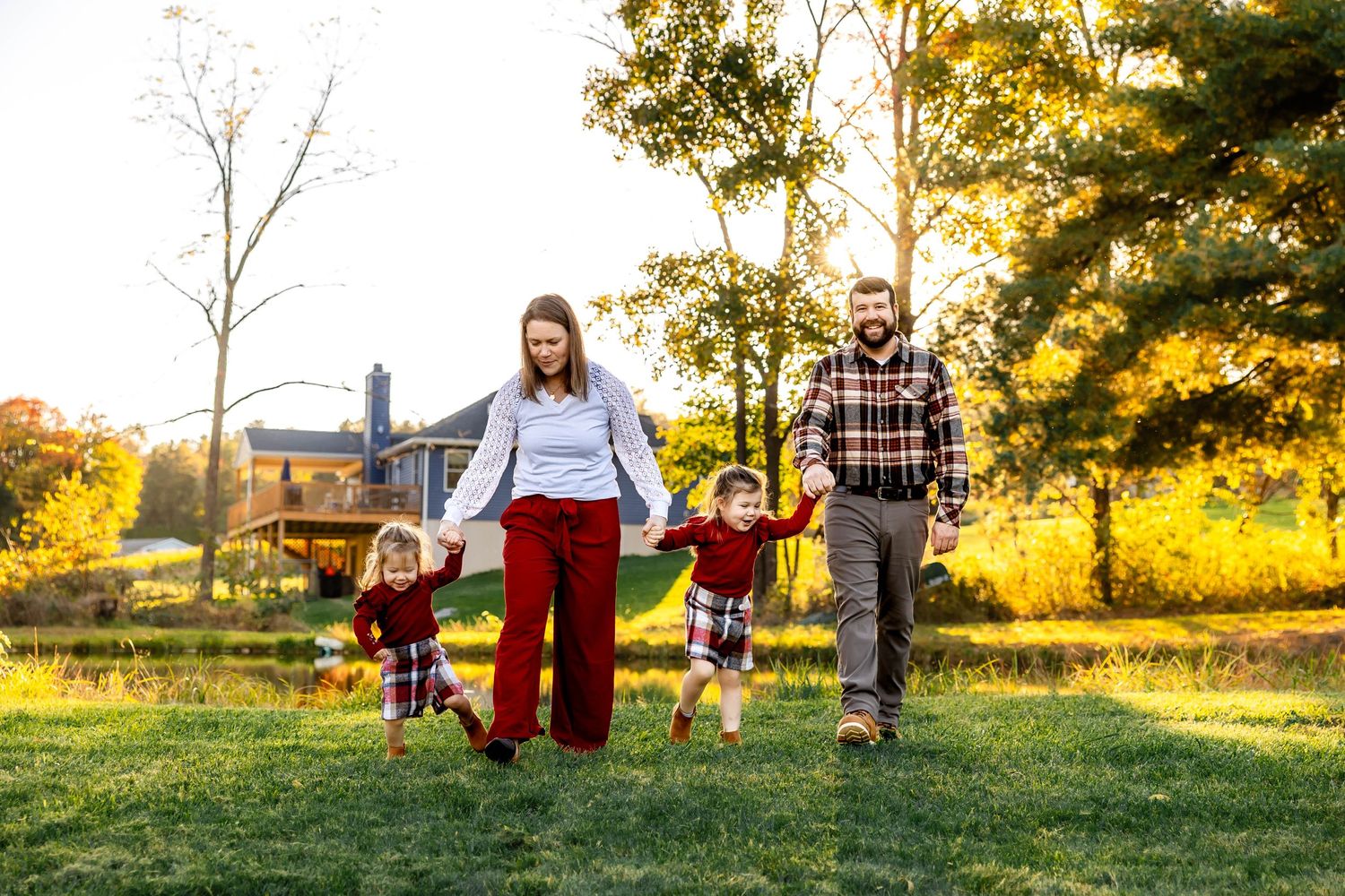 Family walking hand in hand across grassy field during golden hour.