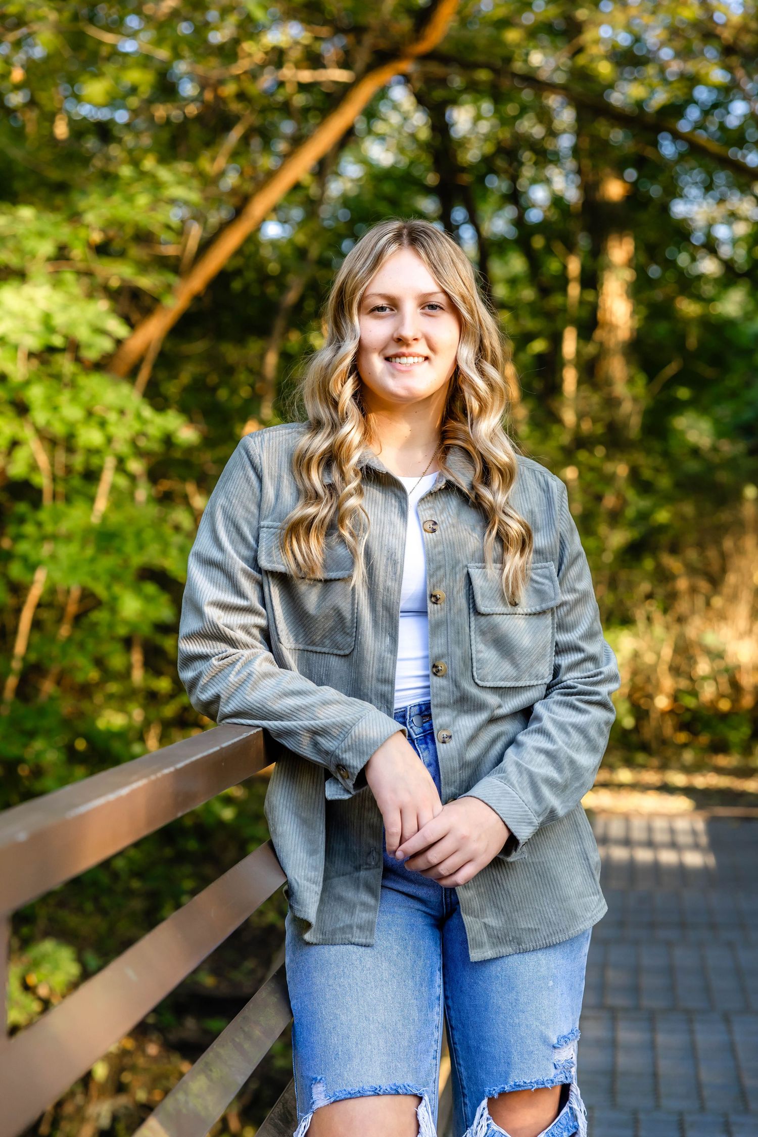 Portrait of person in gray jacket and ripped jeans on wooden bridge with forest background.