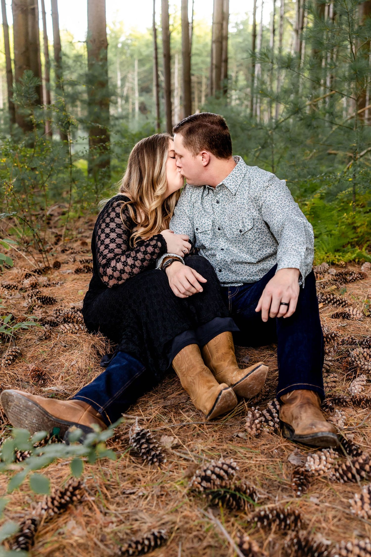 Couple shares an intimate moment while sitting on forest floor covered in pine cones.