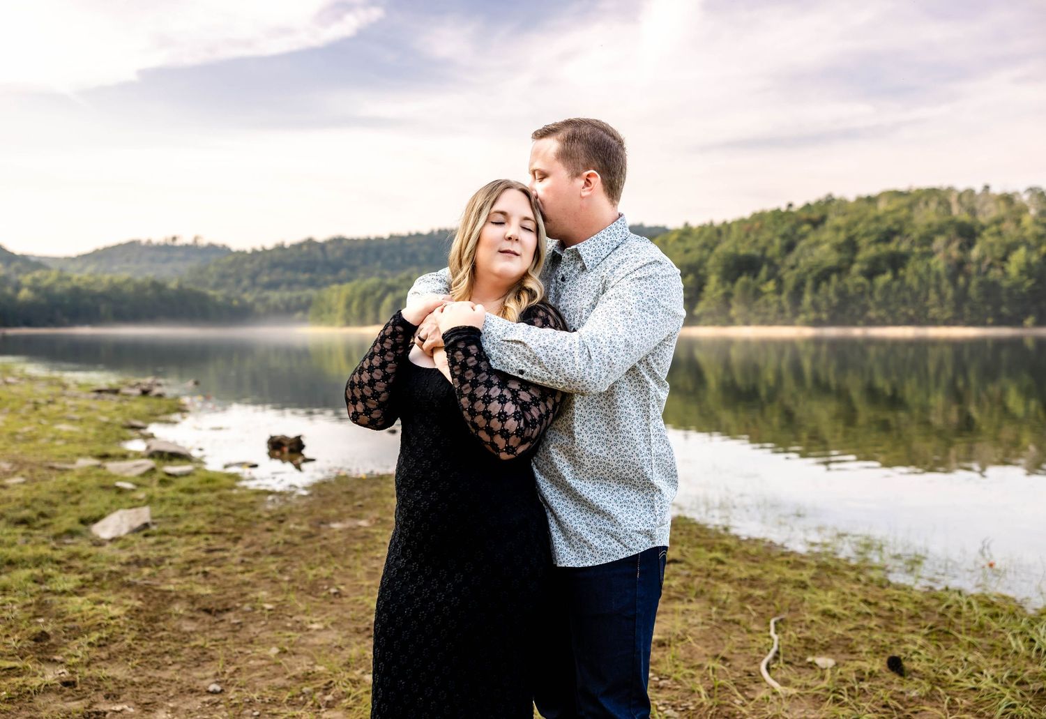 Couple shares intimate moment along lakeside during golden hour engagement session.