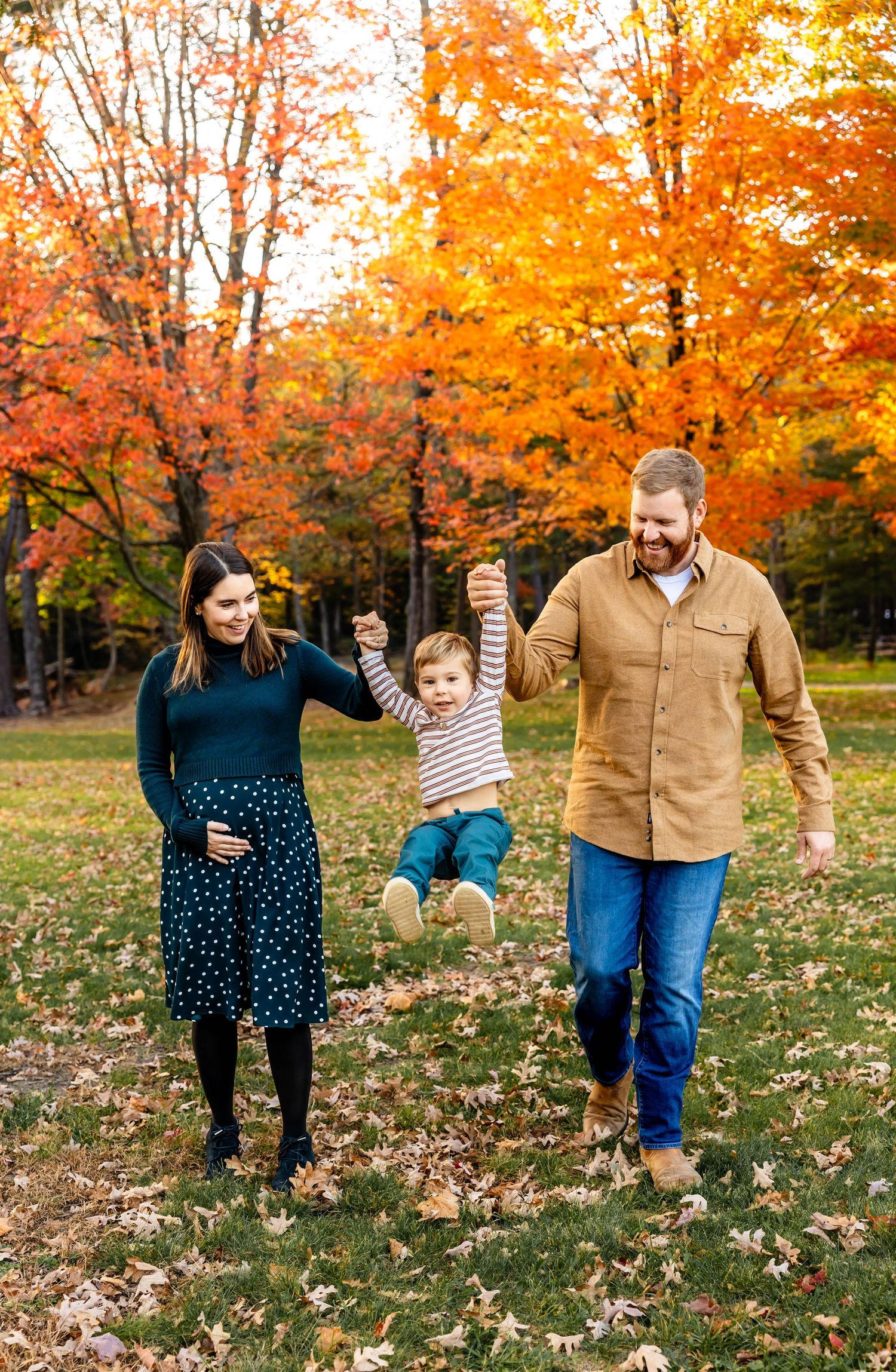 Family playing and swinging child between them in fall park setting.