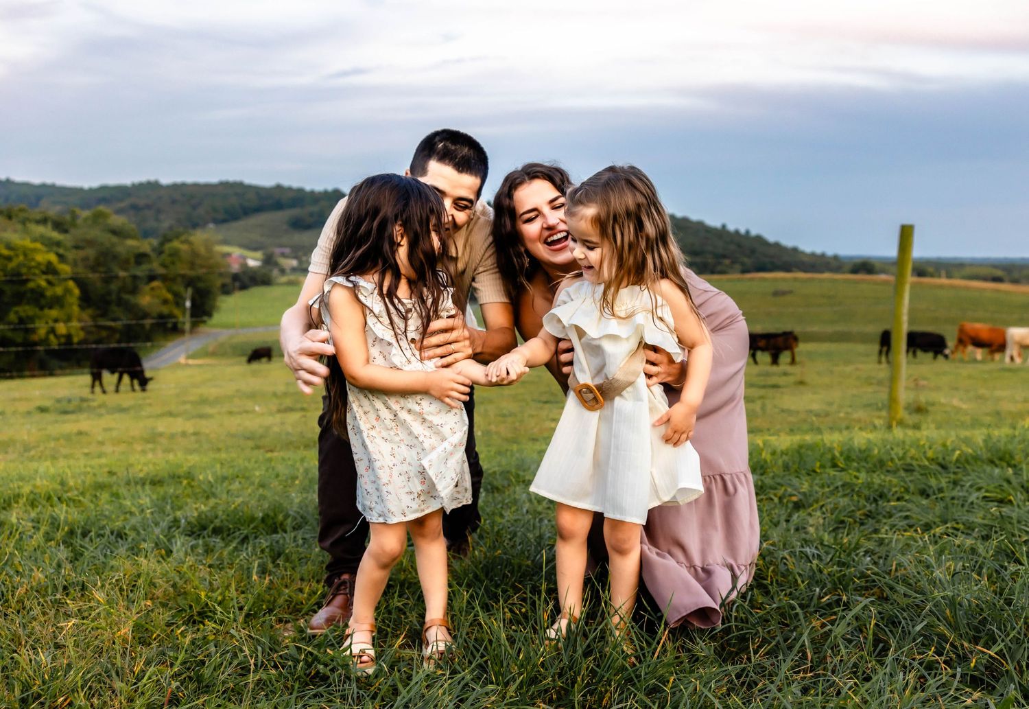 A group shares joyful laughter together on a green hillside with grazing cattle in the background.