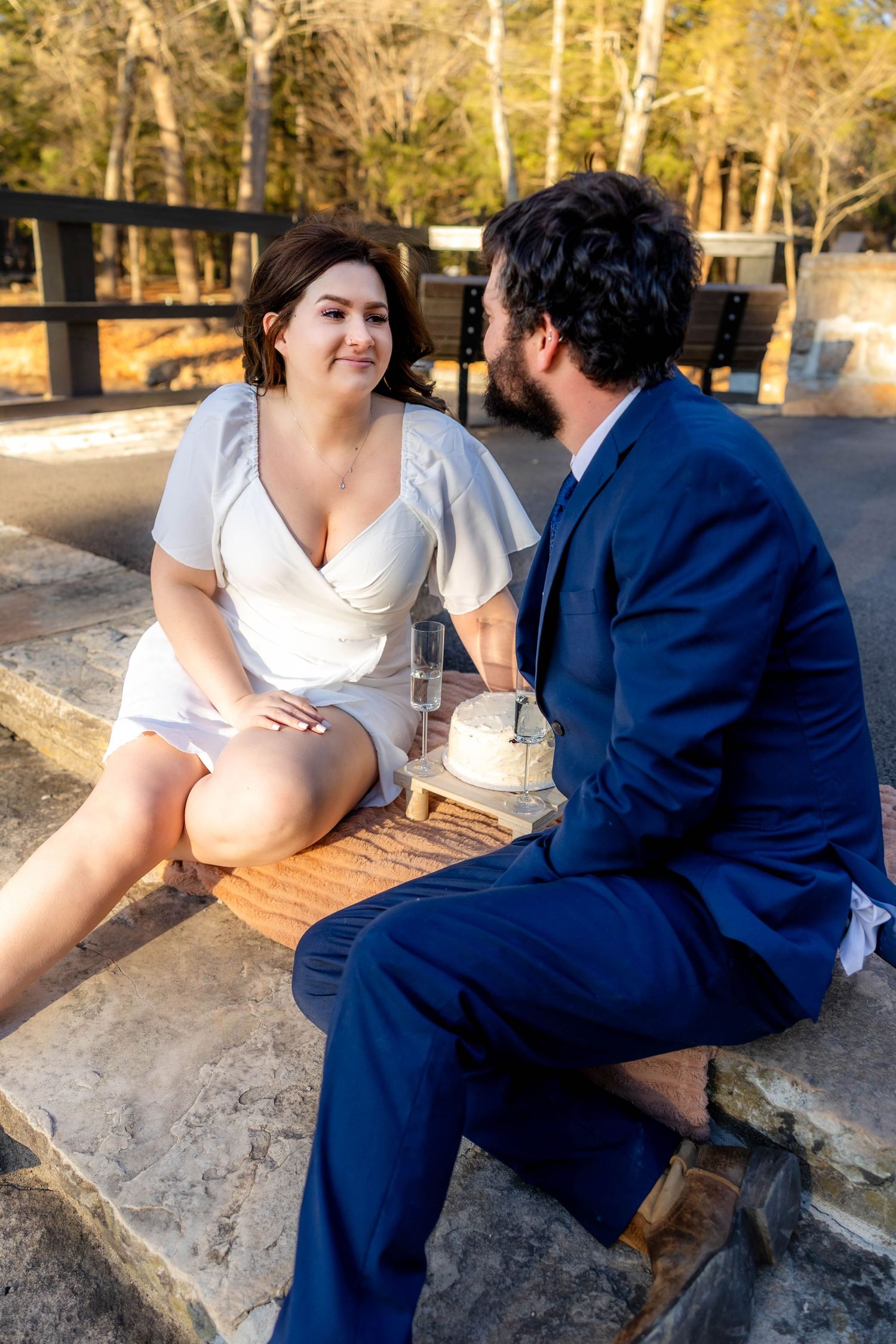 A couple shares a picnic with cake and champagne outdoors.