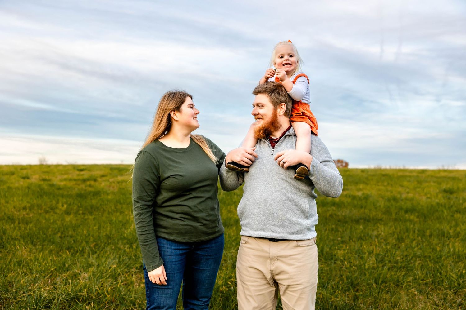 Family enjoying time together outdoors in grassy field with blue sky backdrop.