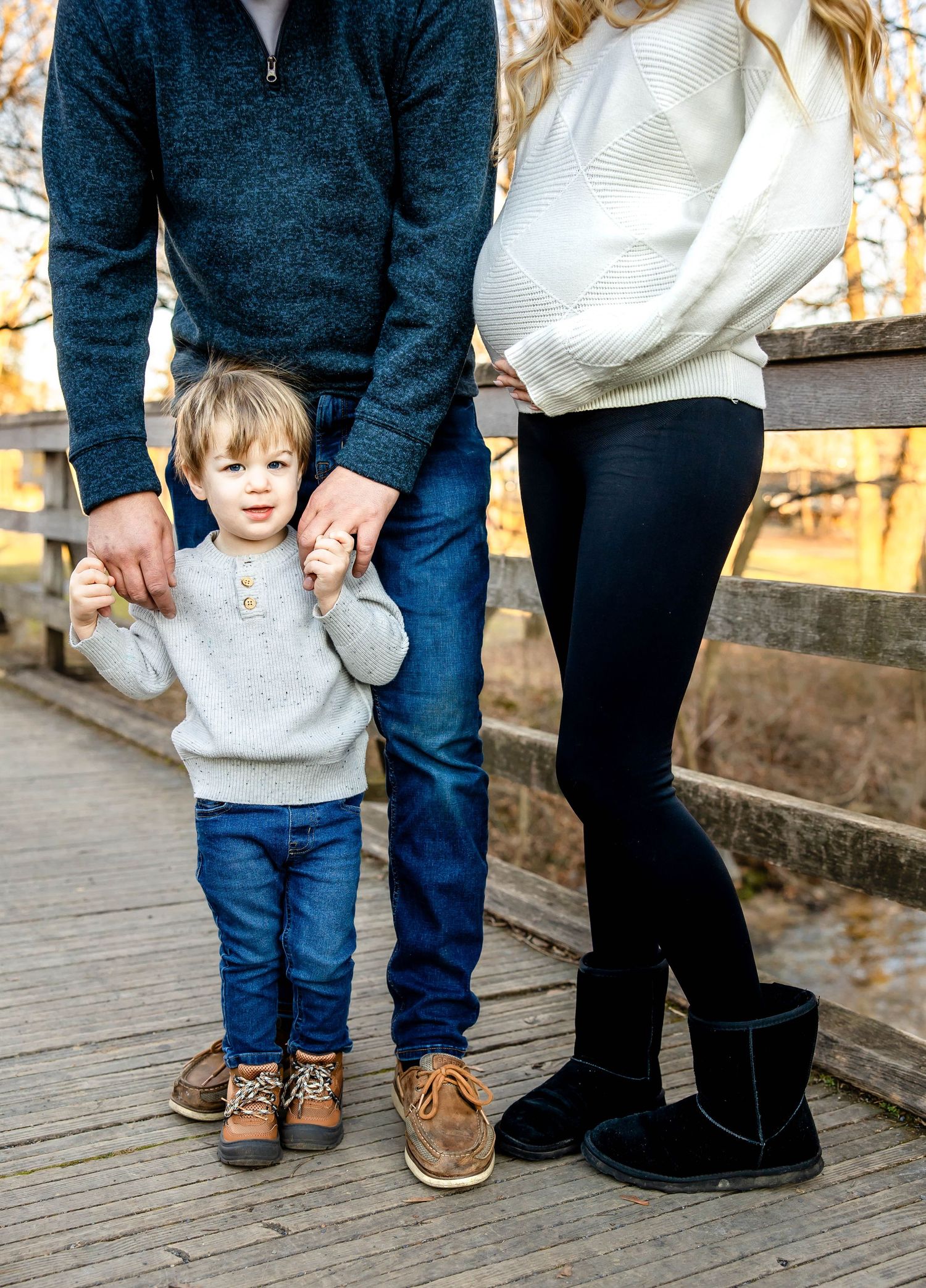 Family photo showing legs and torso of three people standing together on wooden deck.