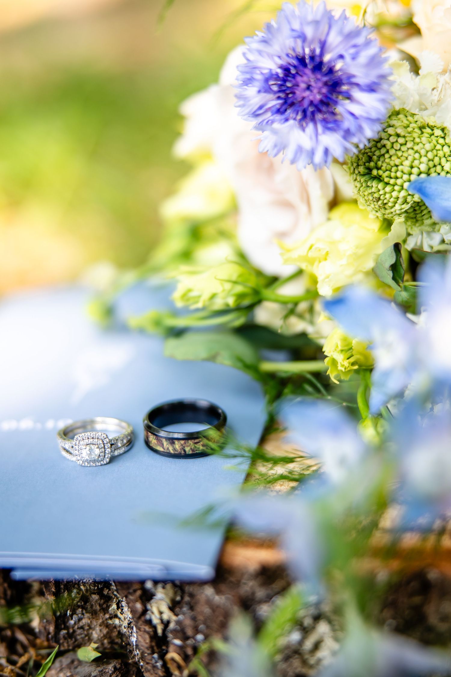 Wedding rings photographed with blue and white flowers in soft focus.