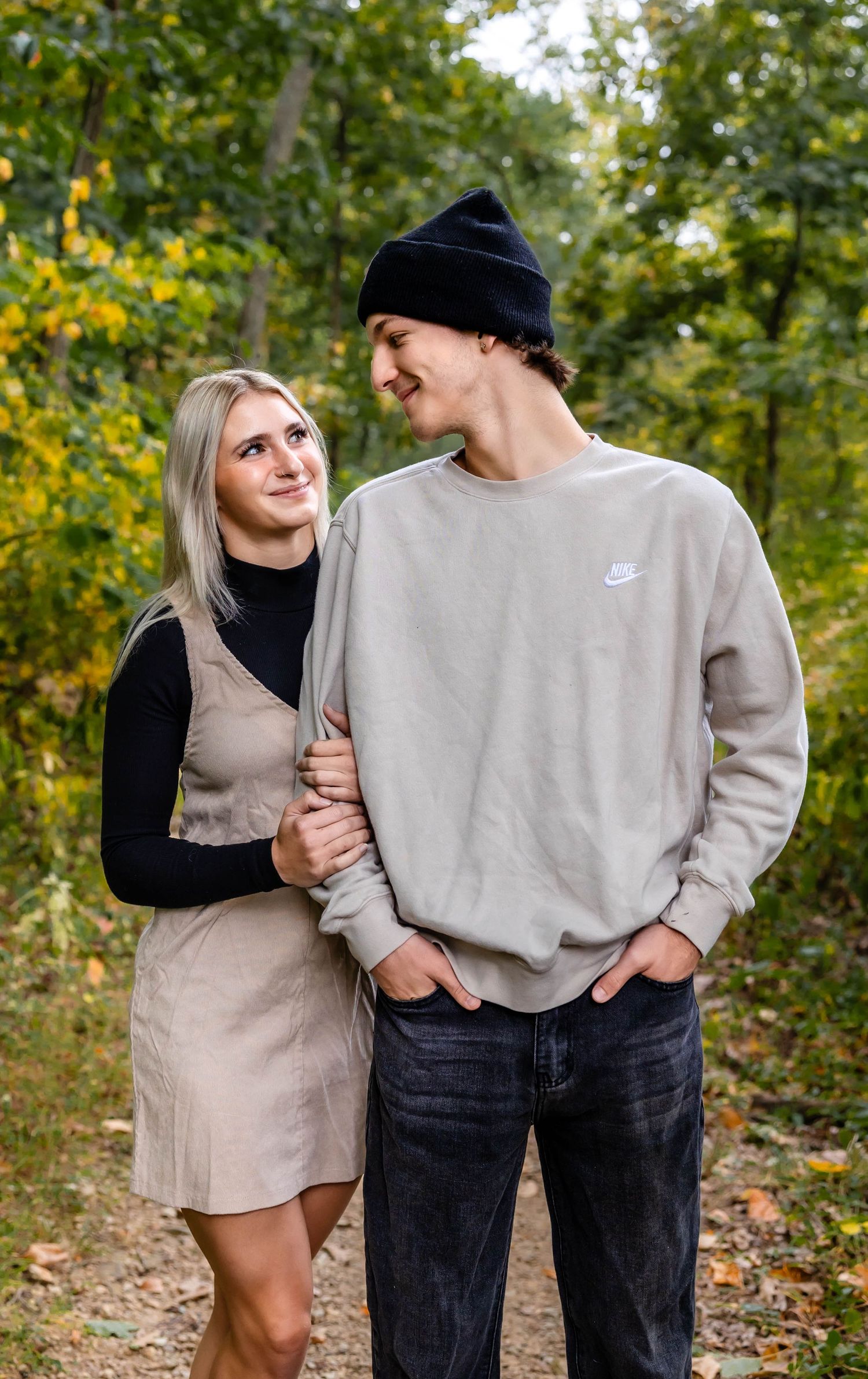 A couple shares a tender moment on an autumn path surrounded by yellow and green foliage.