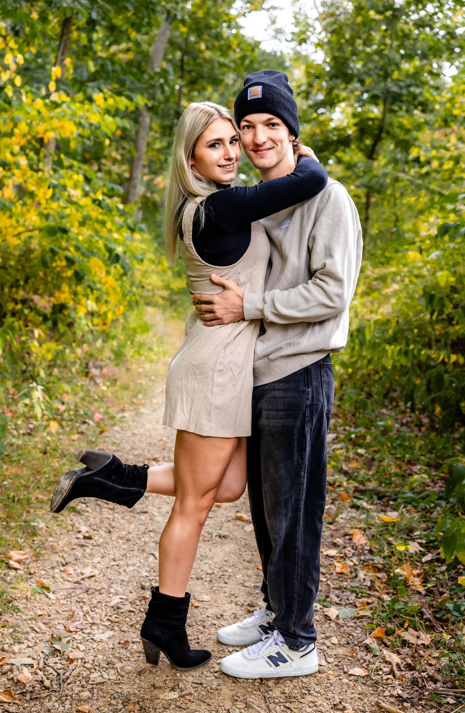 A playful couple poses together on a leaf-covered path during autumn.