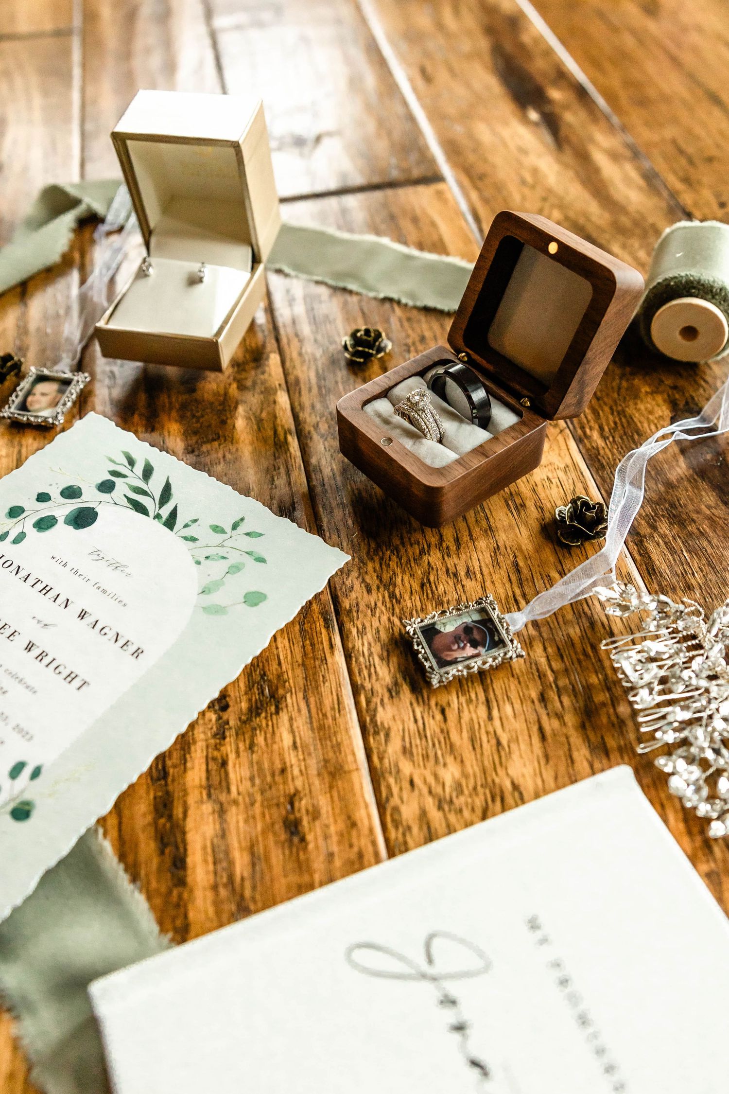 Wedding stationery with greenery design displayed with jewelry boxes on rustic wooden table.