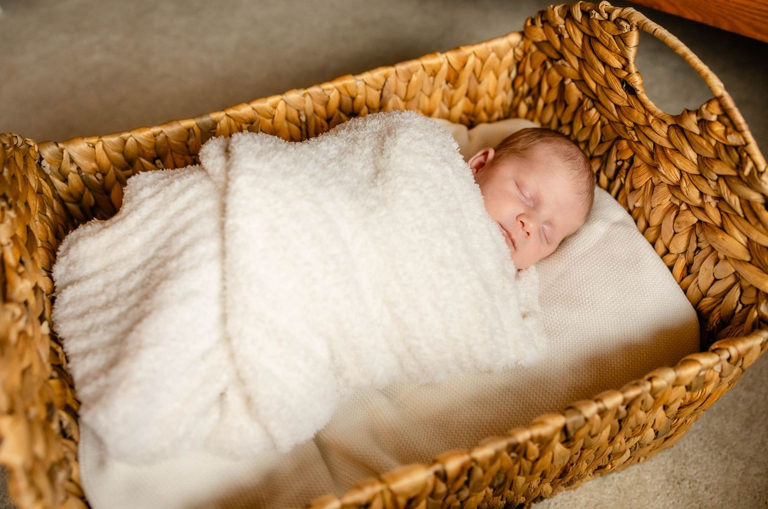 Newborn baby sleeping peacefully in white blanket inside woven basket.