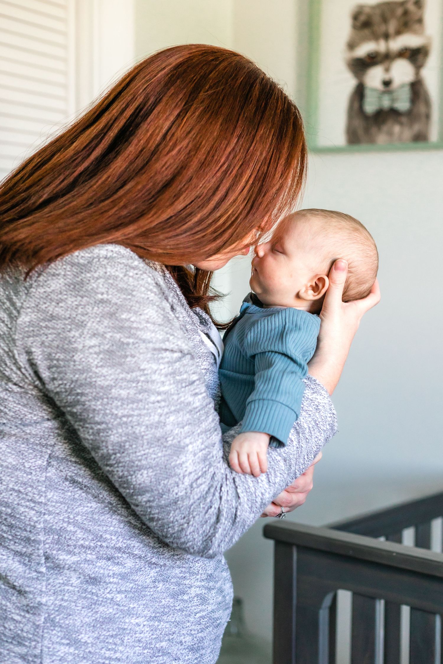 A tender moment between parent and infant wearing a blue sweater beside a nursery crib.