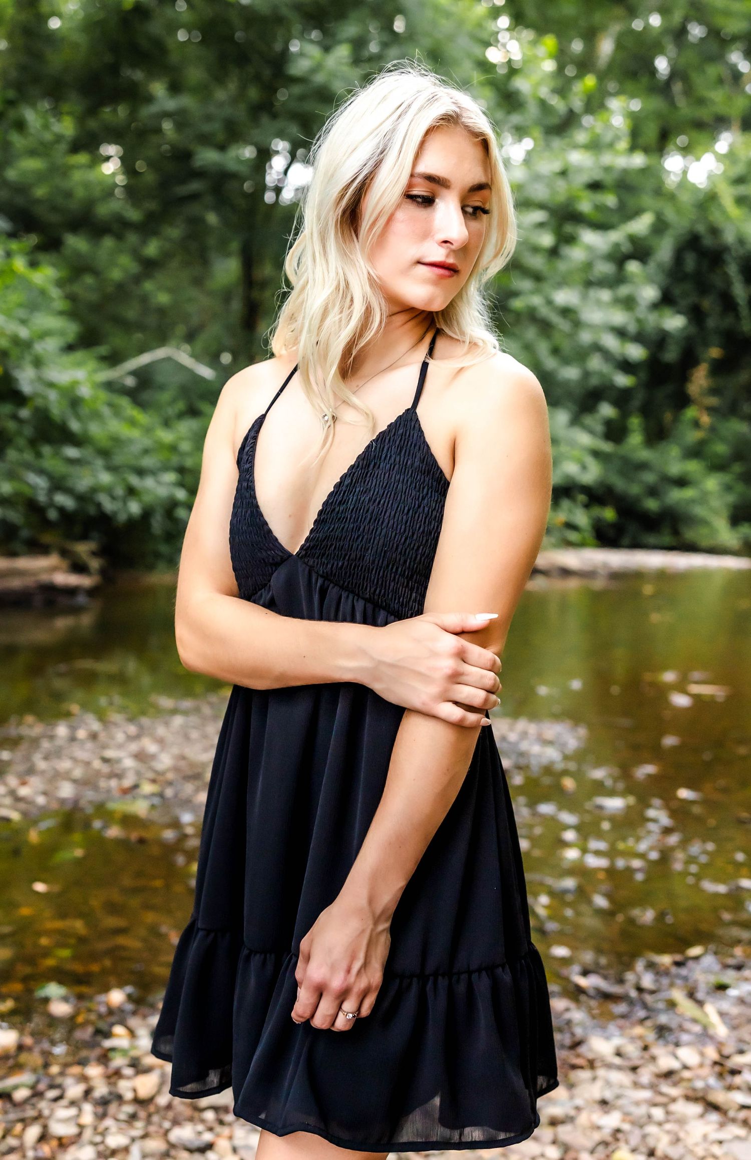 Artistic outdoor portrait with a flowing black dress near a peaceful stream.