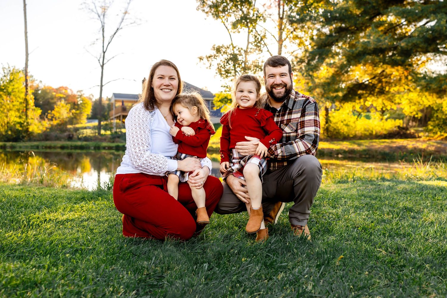Family portrait on grass with autumn foliage and water in background.