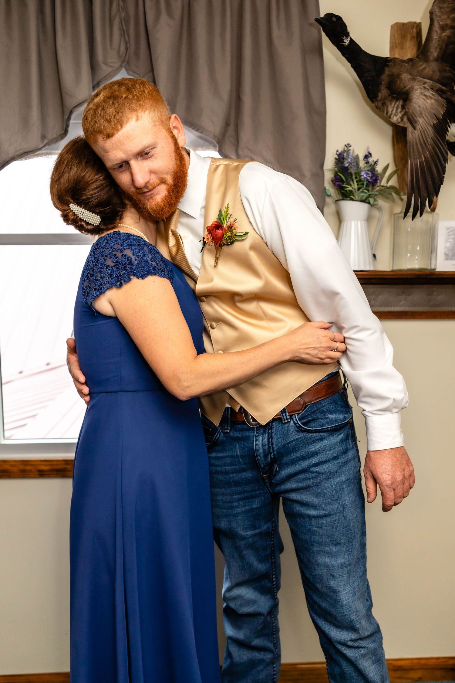 Two people share an embrace while dressed formally with a tan vest and navy blue dress.