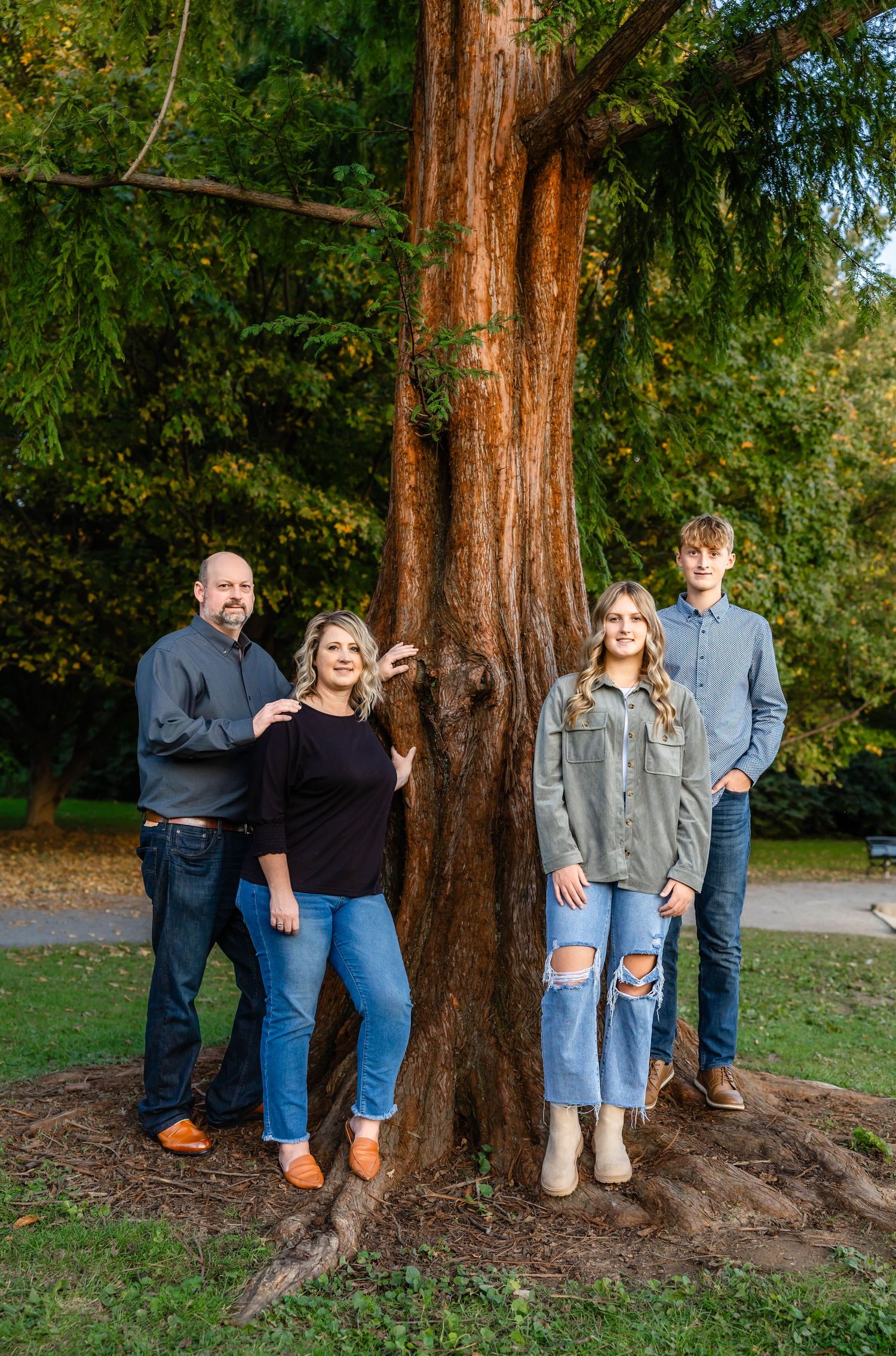 Family portrait by large tree trunk in park during autumn season.