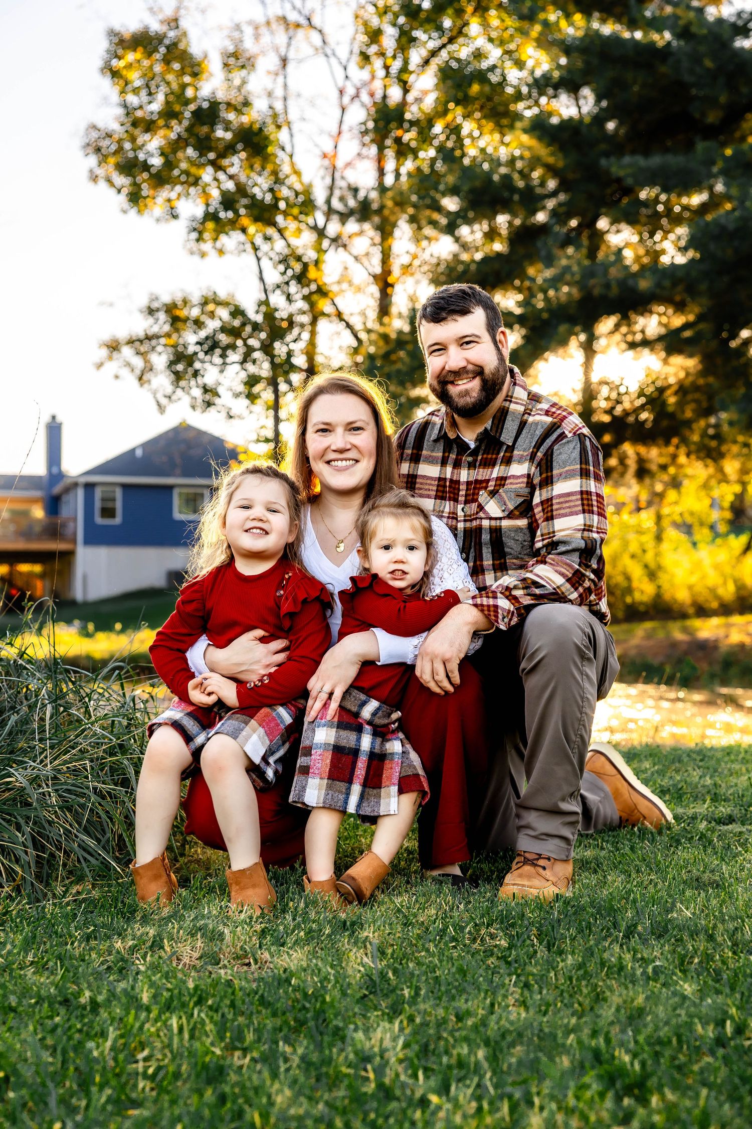 Family of four in coordinated plaid and red outfits pose together on grass during fall photoshoot.