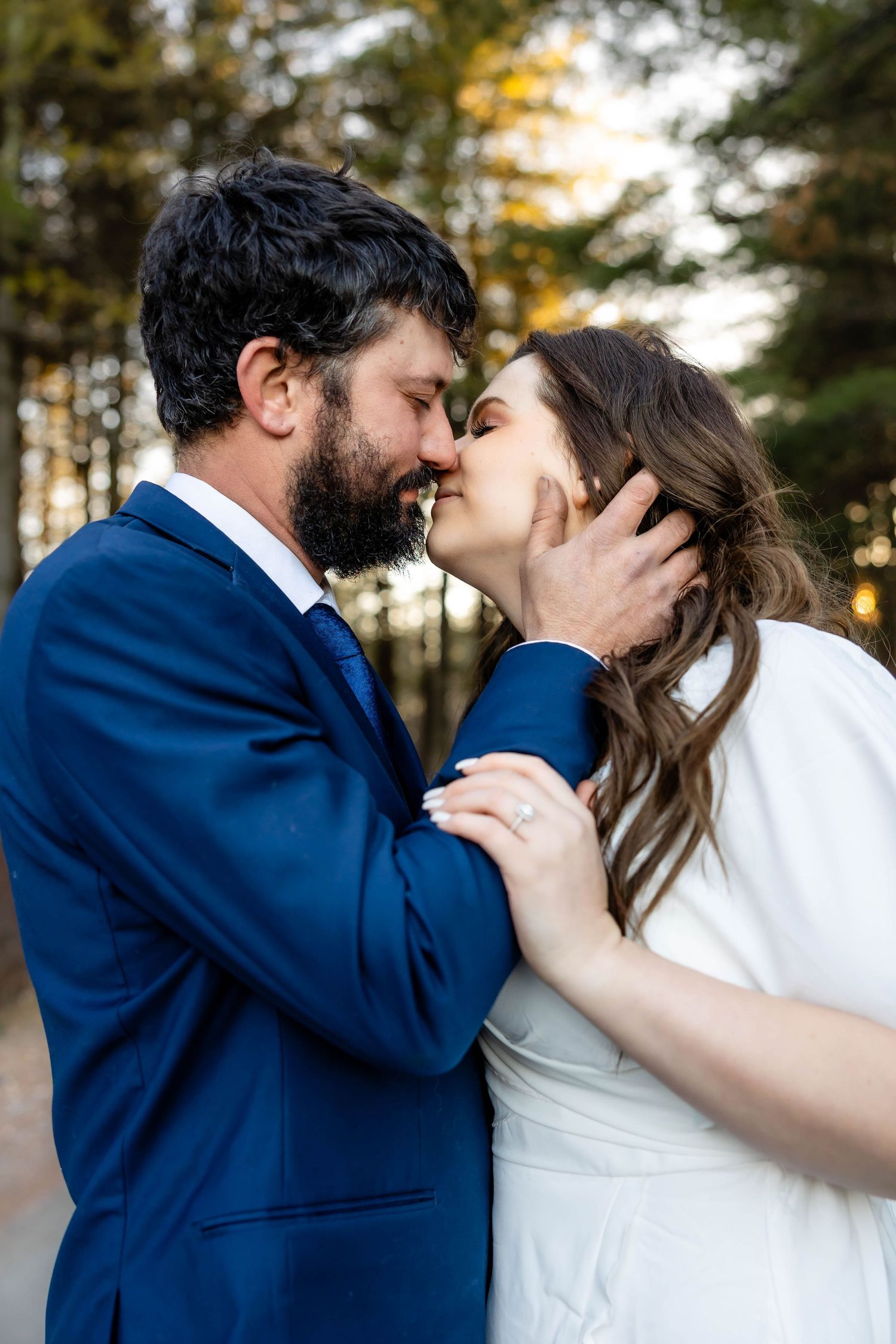 A tender moment between a couple kissing outdoors at sunset, wearing formal attire.