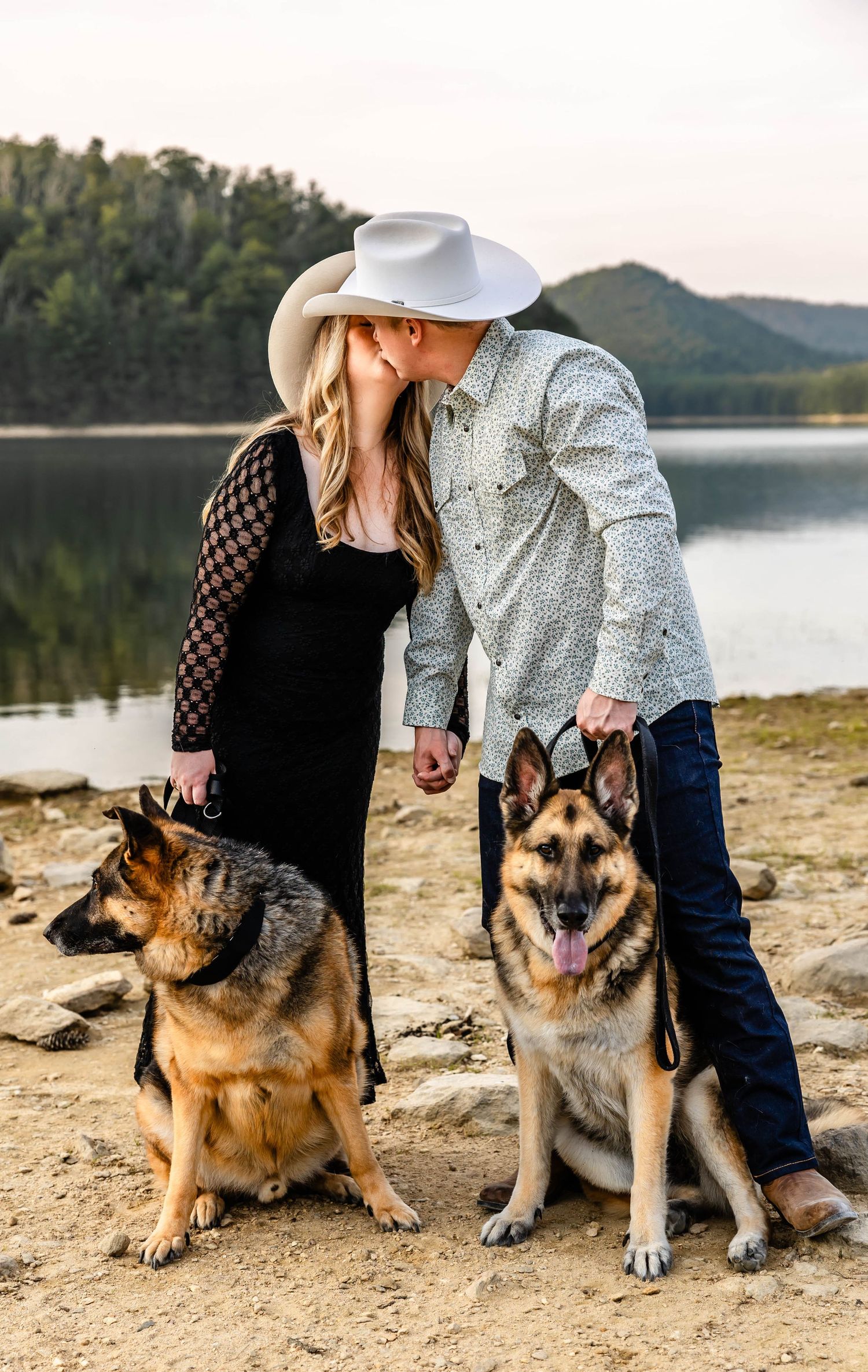 A romantic moment between a couple with their German Shepherd dogs by a mountain lake.