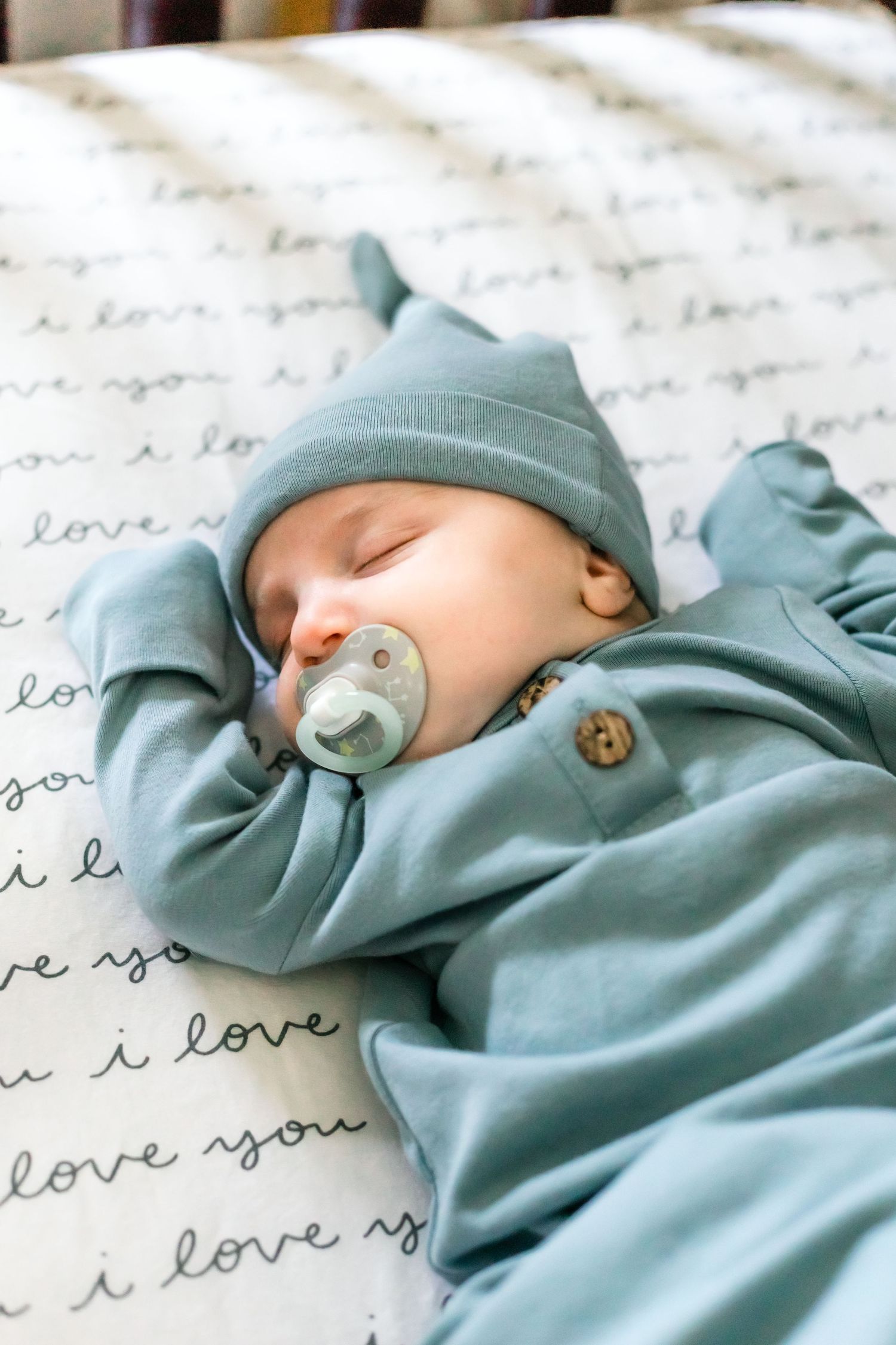 Sleeping infant in blue outfit on blanket with 'love' text pattern.