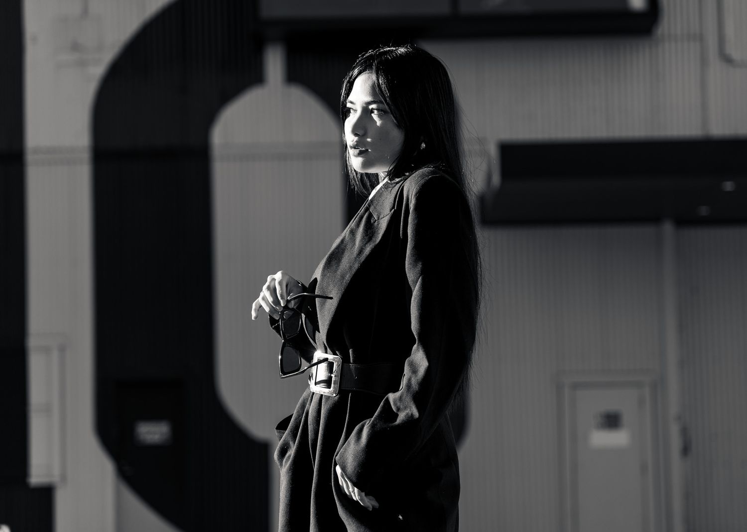 Black and white portrait of a woman in a dark coat standing in a dramatic industrial setting.