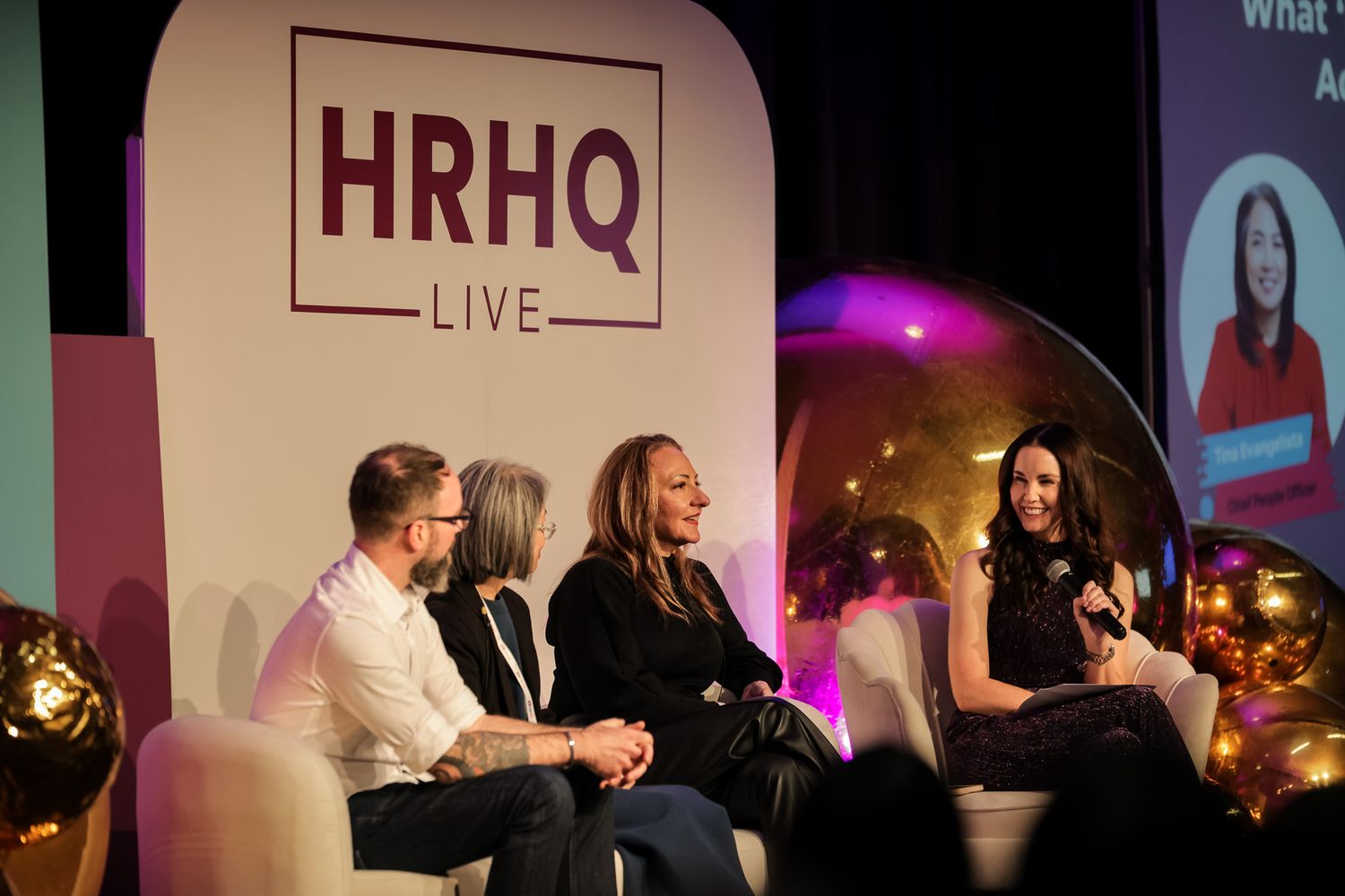 Four panelists seated on stage at HRHQ Live event, engaged in discussion under branded signage.