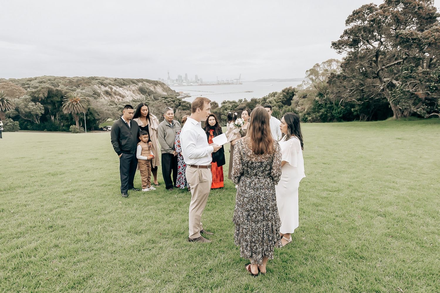 Small outdoor wedding ceremony on green lawn with guests gathered around couple.