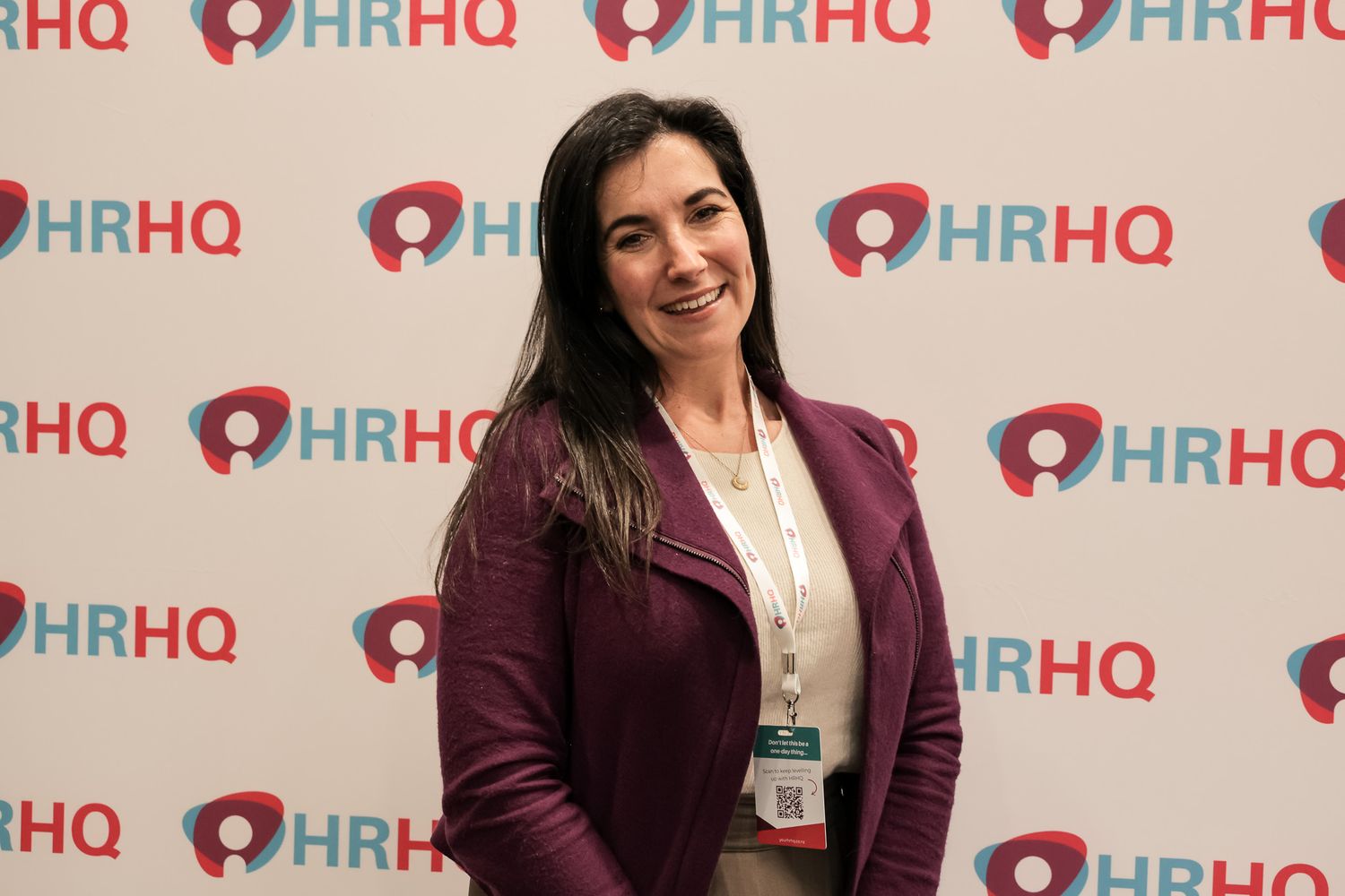 Woman in burgundy blazer smiling at HRHQ conference event backdrop.