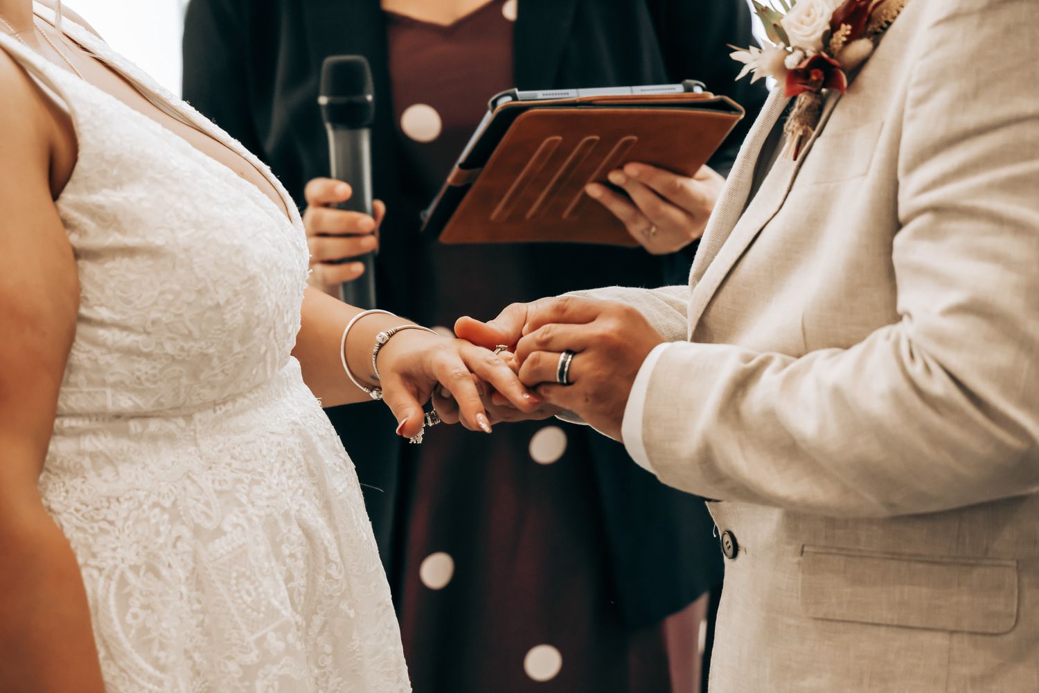Couple exchanging wedding rings during an intimate ceremony with officiant holding microphone.