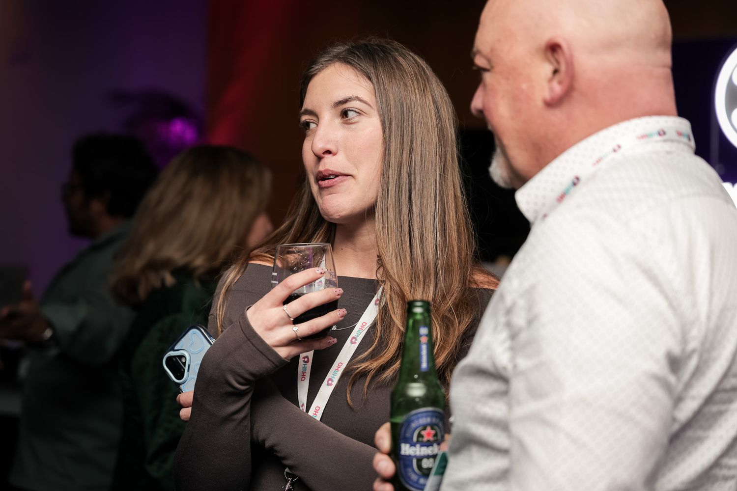 Two people networking at an event, woman holding a drink and man with a beer bottle in conversation.