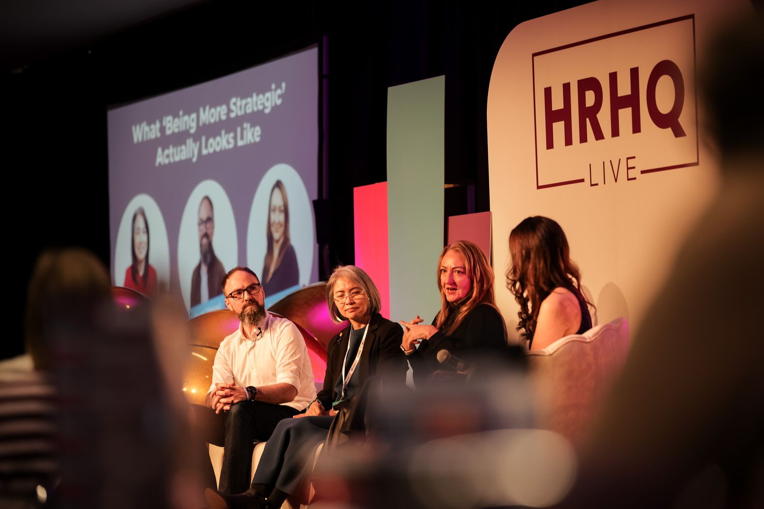 Panel discussion at HRHQ Live event with four speakers seated on stage beneath a presentation screen.