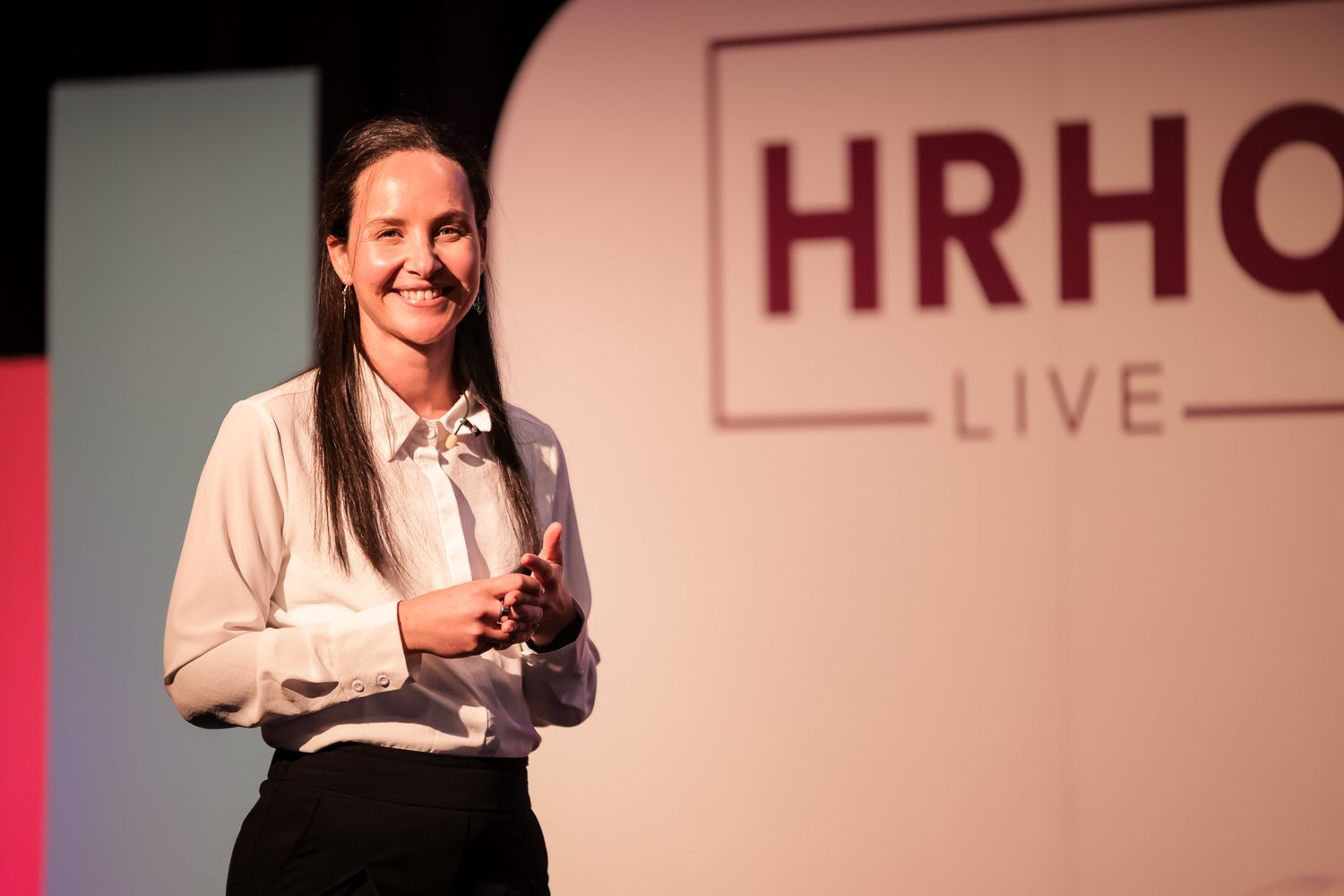 Woman presenting on stage at HRHQ Live event, smiling confidently in professional attire.