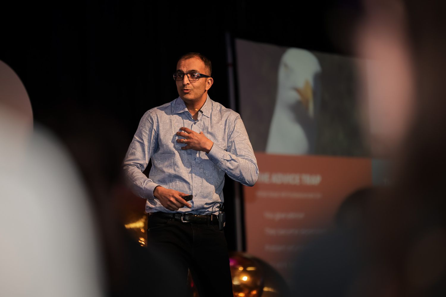 A man in a striped shirt presents at a conference with a projected eagle slide behind him.