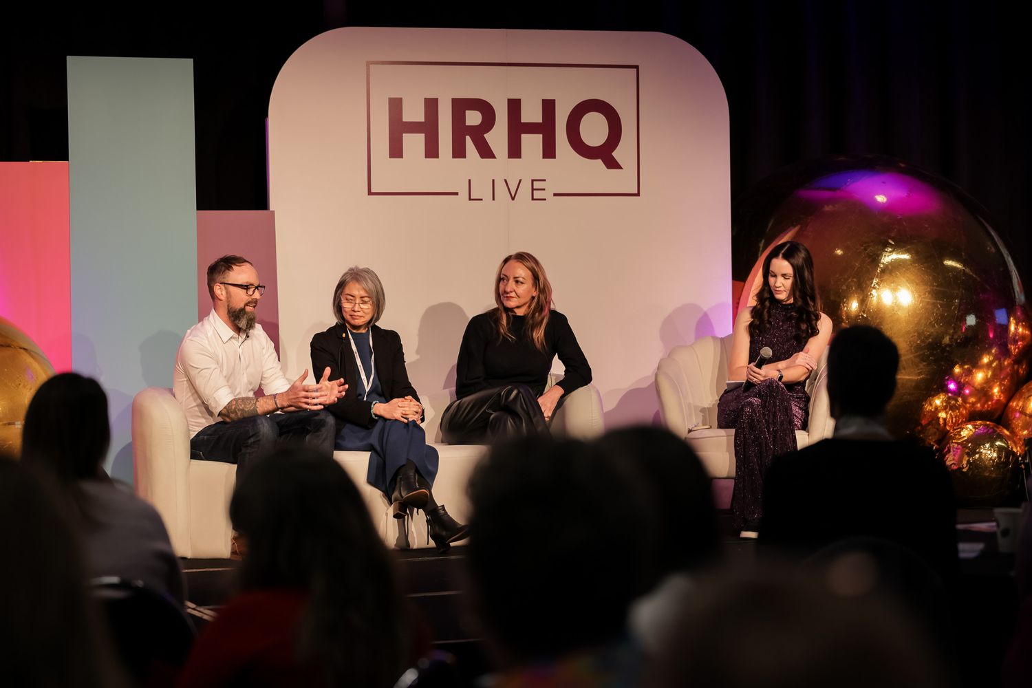Four panelists seated in white chairs on stage at HRHQ Live conference event.