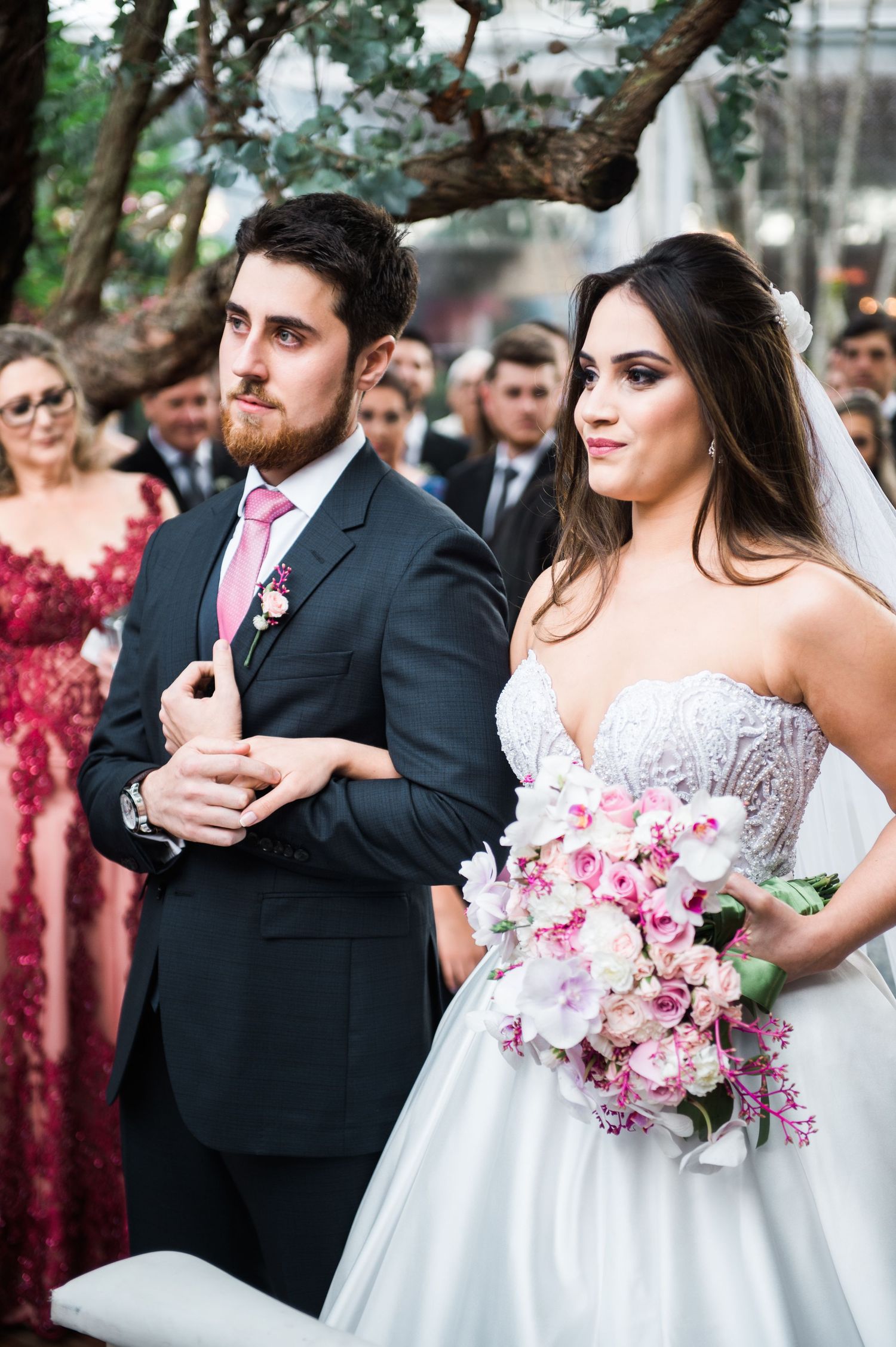 Wedding couple embraces while holding a pink and white bouquet in an outdoor garden setting.