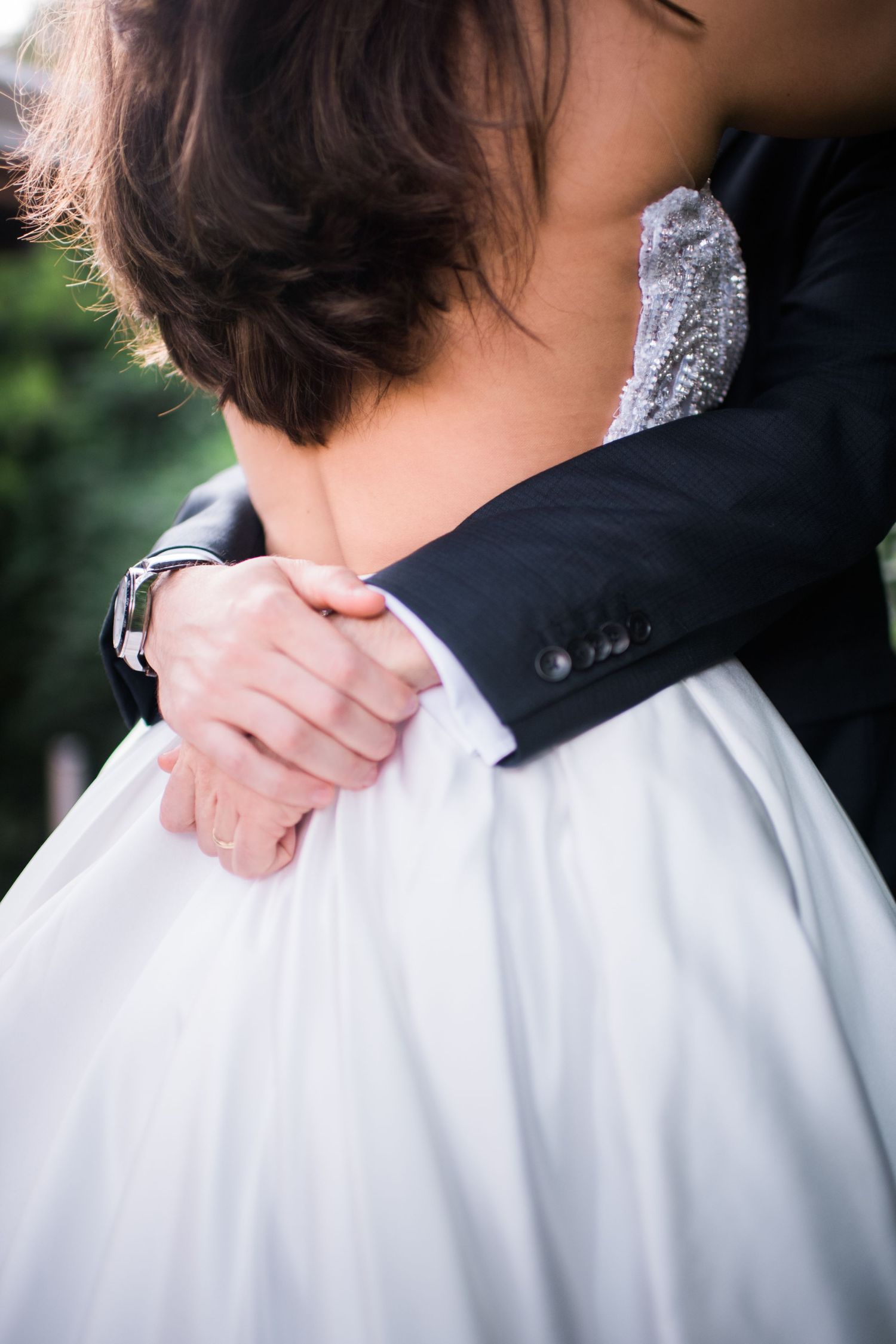 Close-up details of bride and groom embracing, showing white dress and black suit.