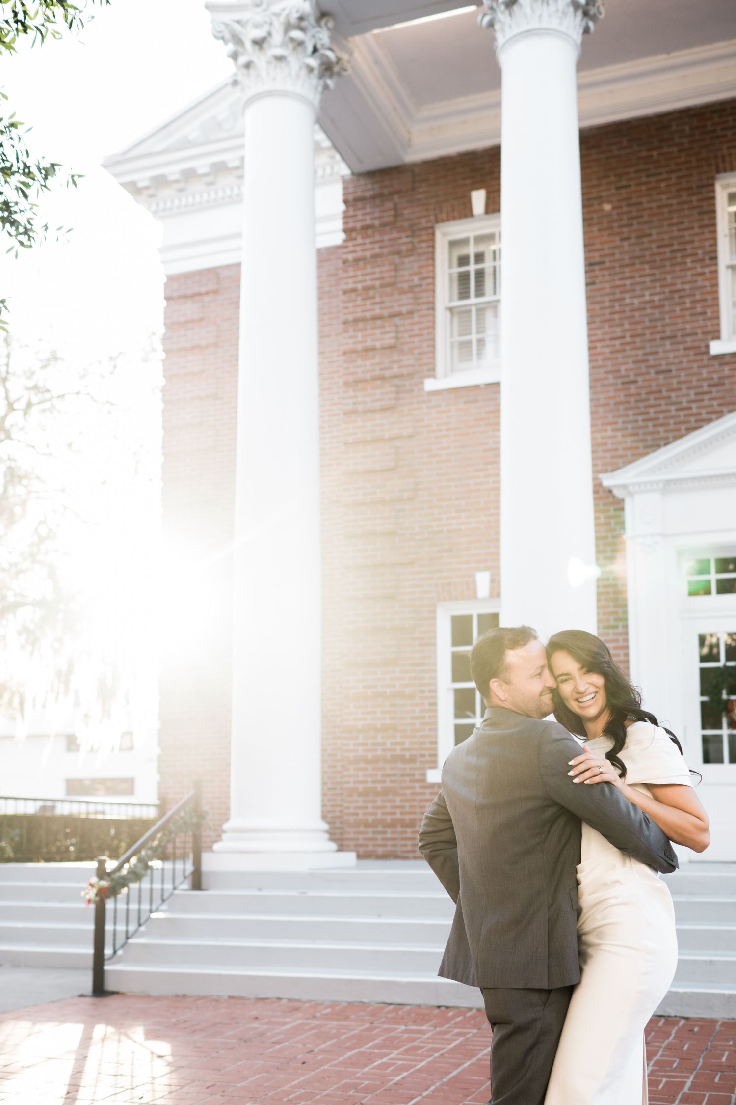 A romantic embrace captured in sunlight between white columns of a historic building.
