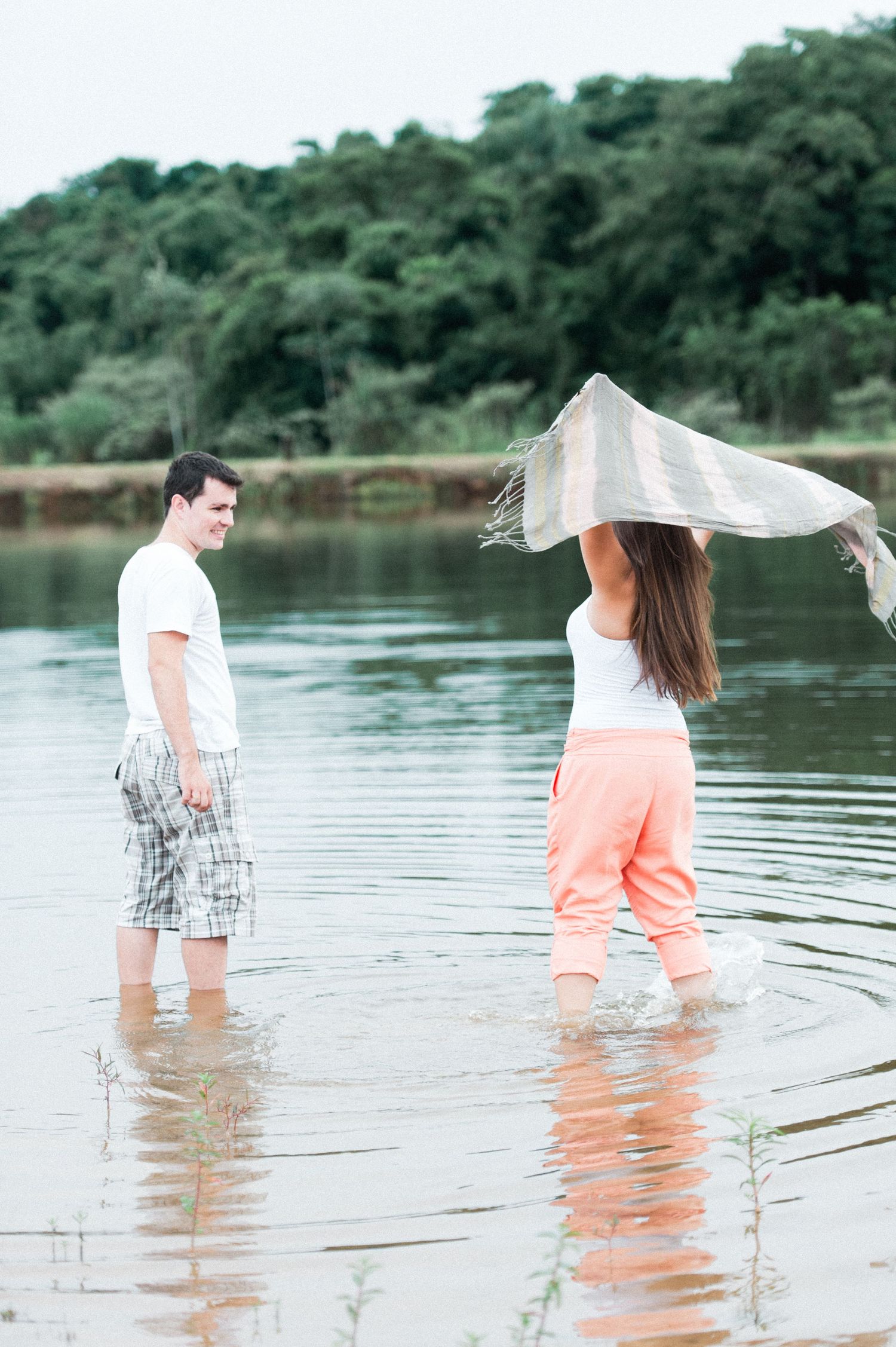 Couple wading in lake water with flowing fabric in breeze.