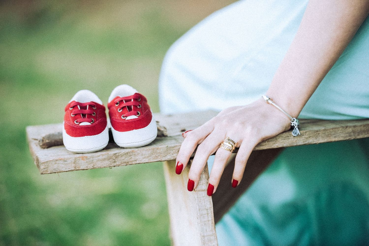 Detail shot of red and white baby shoes on wooden bench during maternity session.