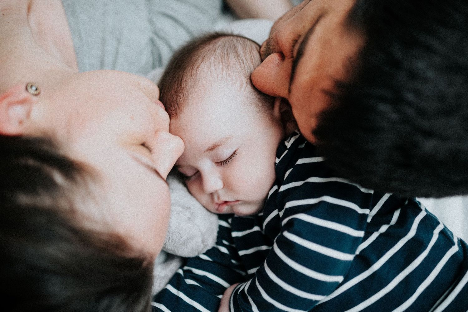 Parent and baby in striped outfit share intimate bonding moment.