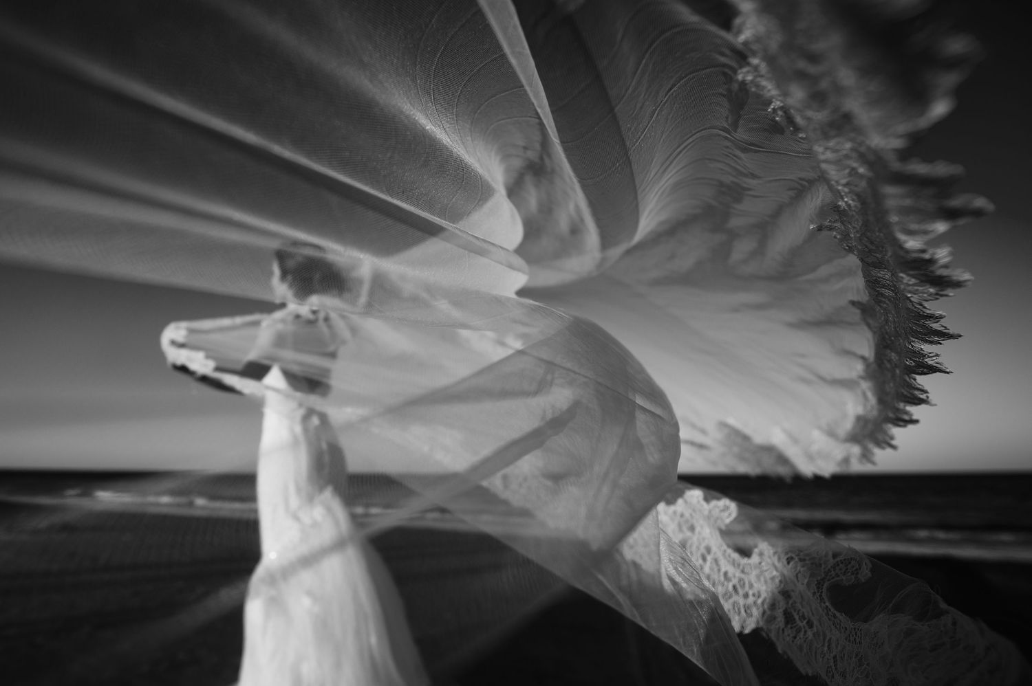 Ethereal wedding veil flowing in the wind against dramatic sky.