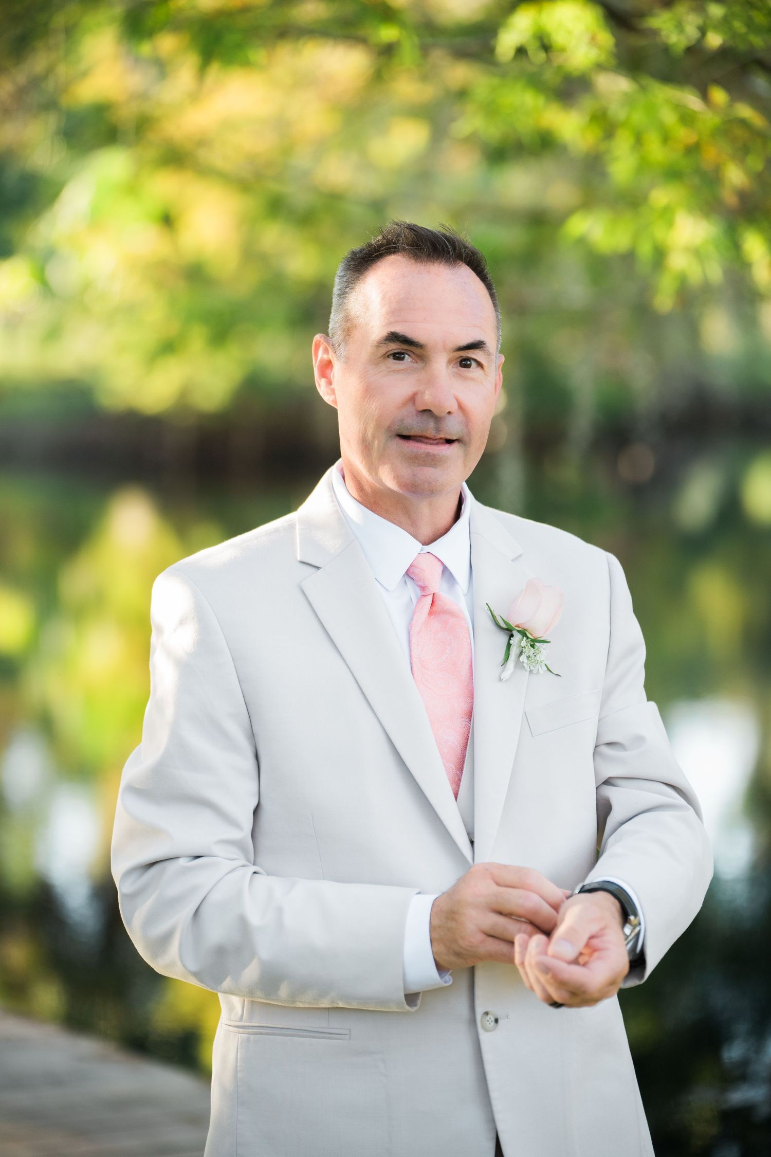 Groom wearing light colored suit adjusts sleeve during outdoor wedding photoshoot.