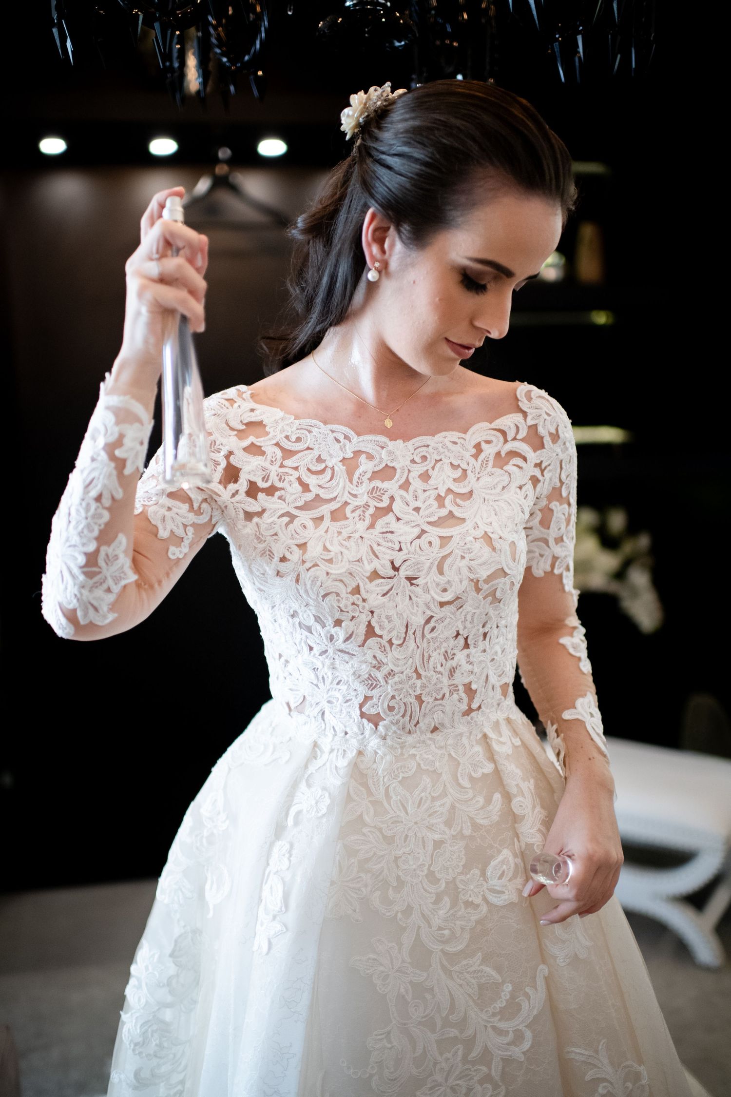 Dramatic shot of a white lace wedding dress with off-shoulder neckline against dark background.